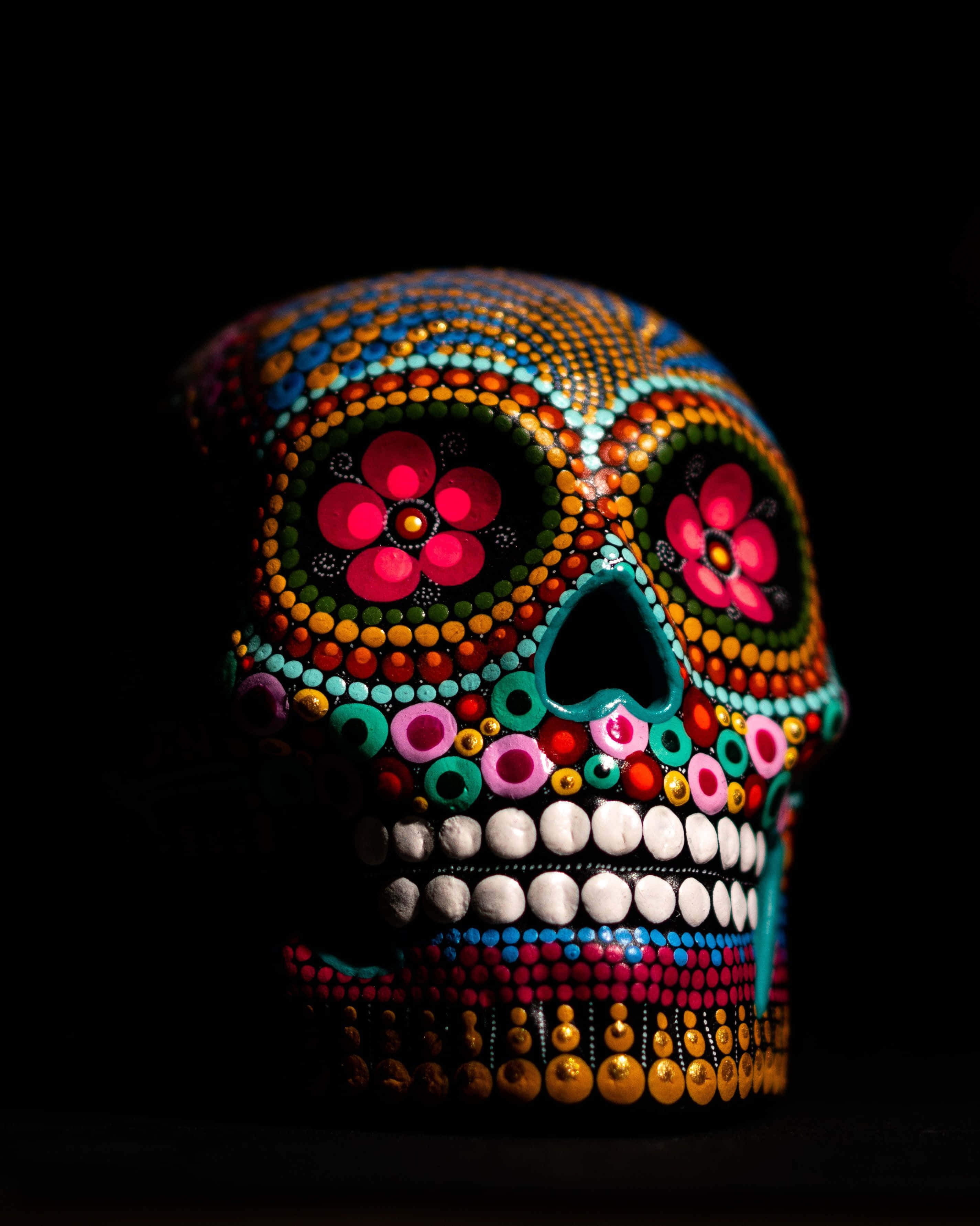 Day Of The Dead 桌布 壁紙 — 一個色彩鮮豔的糖骷髏，飾有彩色圓點和花朵，在純黑背景下閃耀。