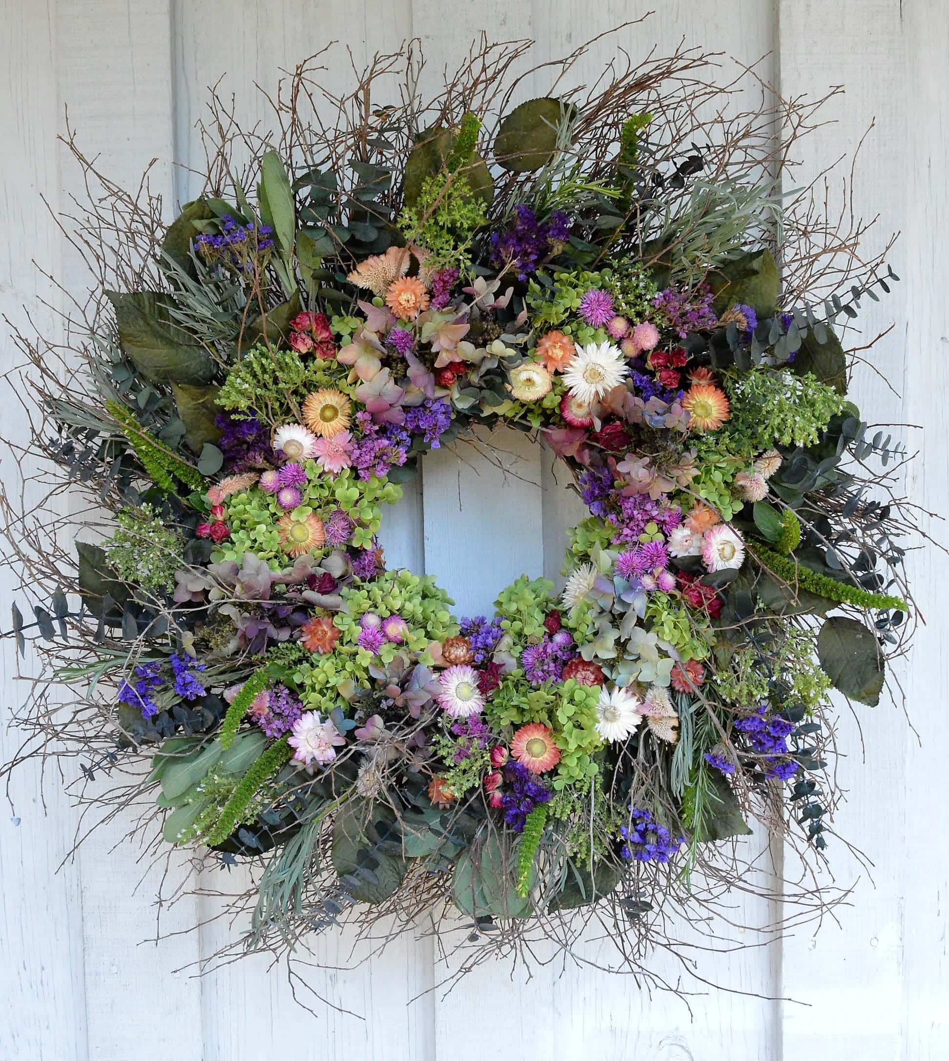 Spring Wreaths 桌布 壁紙 — 一個茂盛的花環，充滿紫色、粉紅色和橙色的花朵和綠葉，掛在白色的木門上。