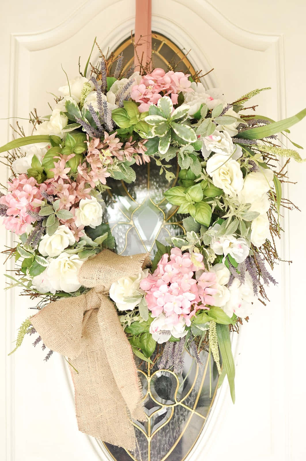 Spring Wreaths 桌布 壁紙 — 一個茂盛的花環，帶有粉白色花朵和綠葉，掛在帶有彩色玻璃窗的白色門上。