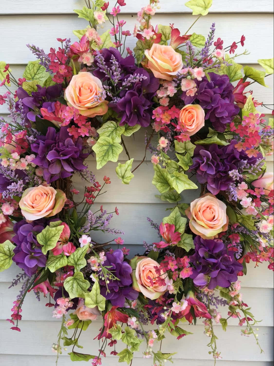 Spring Wreaths 桌布 壁紙 — 一個茂盛的花環，有蜜桃玫瑰、紫色繡球花和薰衣草花朵，掛在淺灰色牆板上。