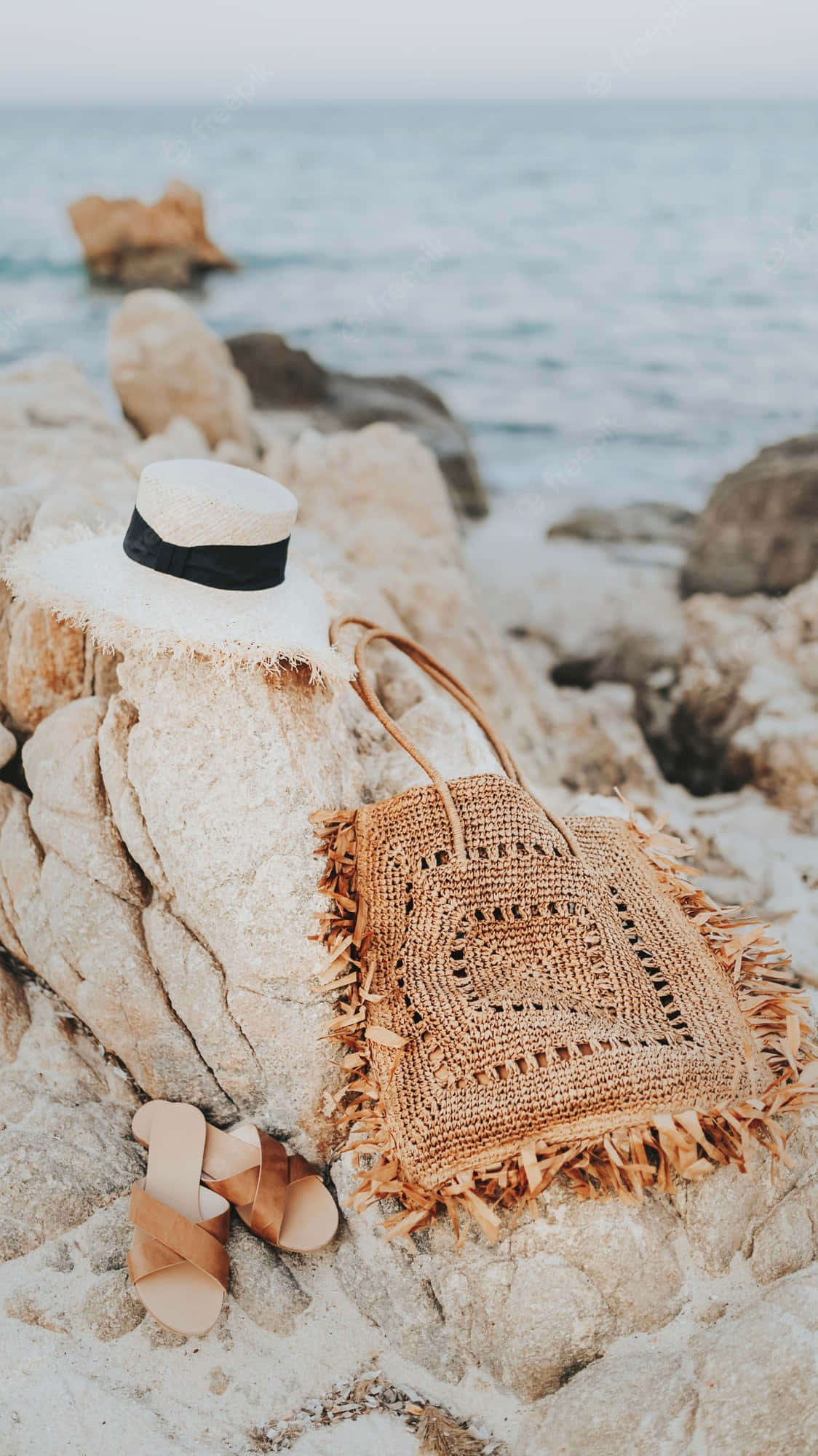 Beach Hat 桌布 壁紙 — 一個草編帽袋和涼鞋放在陽光照耀的海邊岩石上，旁邊是海洋。