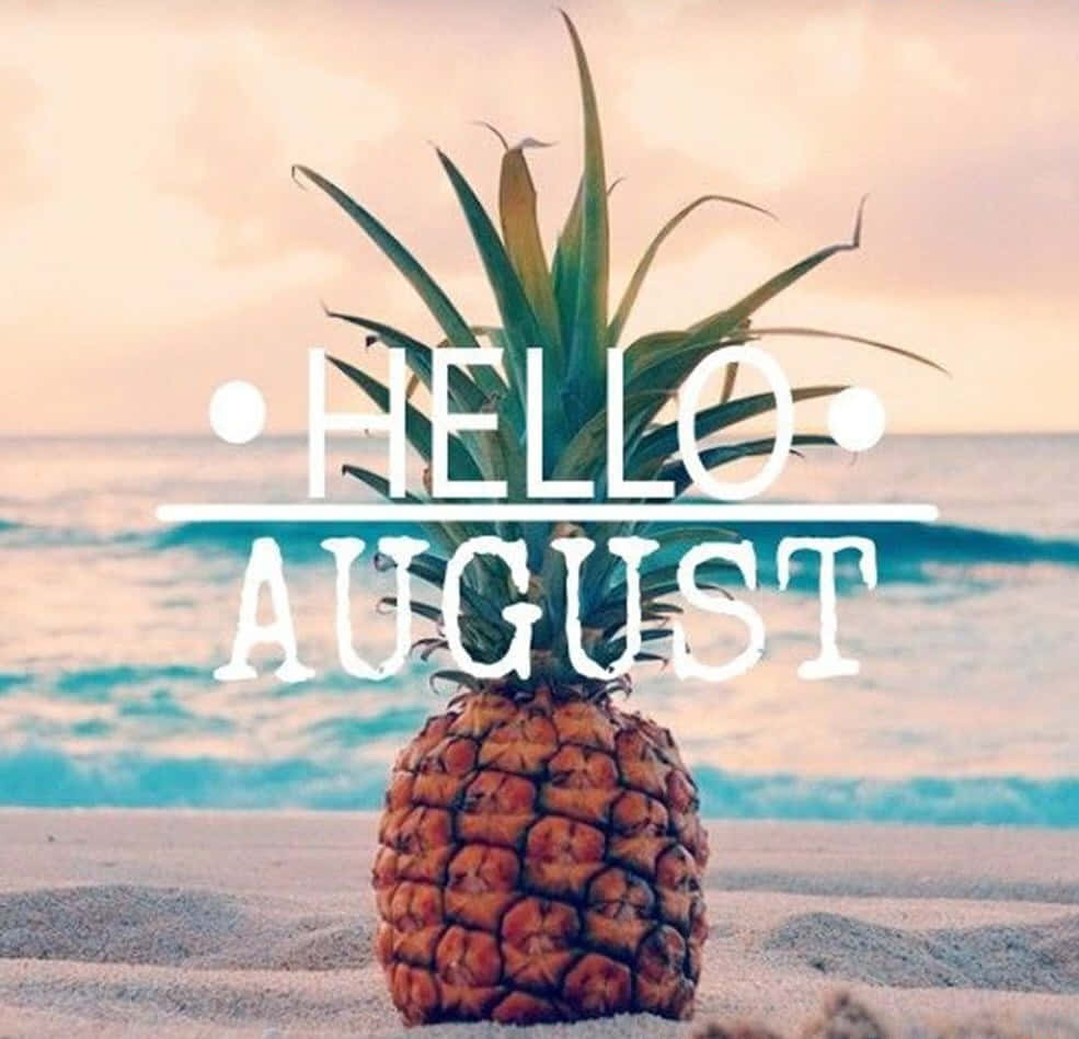 August 桌布 壁紙 — 一個菠蘿放在沙灘上，背後有海浪和日落天空，並帶有 'HELLO AUGUST' 文字疊加。