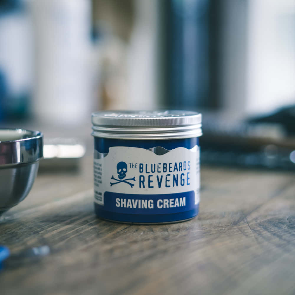 Shaving Cream 桌布 壁紙 — 一個藍白相間的「The Bluebeards Revenge」剃鬚膏罐放在木質表面上，旁邊有一個模糊的金屬碗。