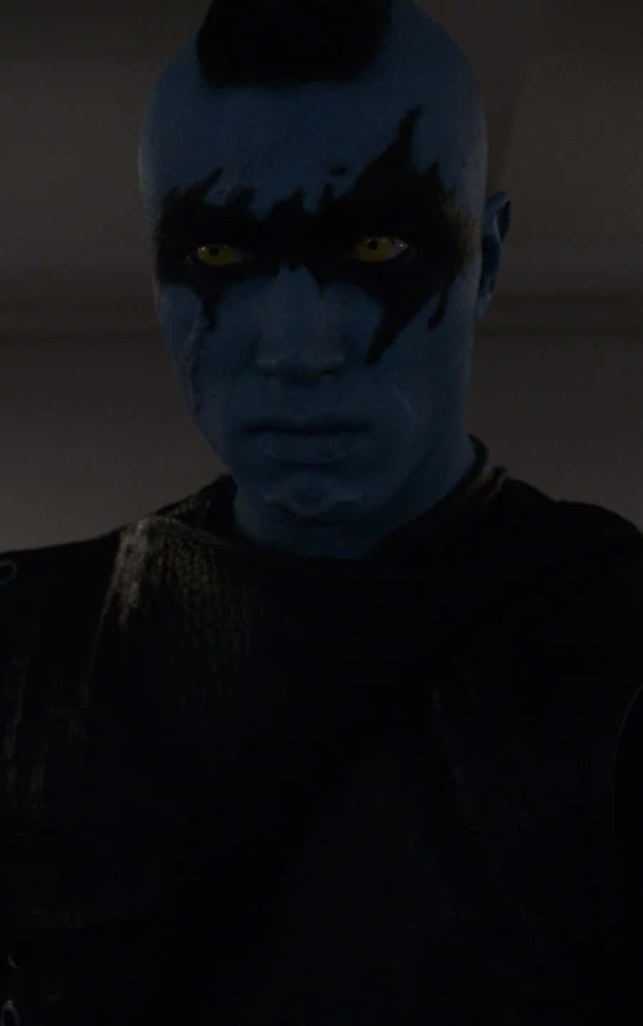 Kree 桌布 壁紙 — 一個藍皮膚、發光黃眼睛和黑色面部標記的外星人在昏暗光線下強烈凝視。
