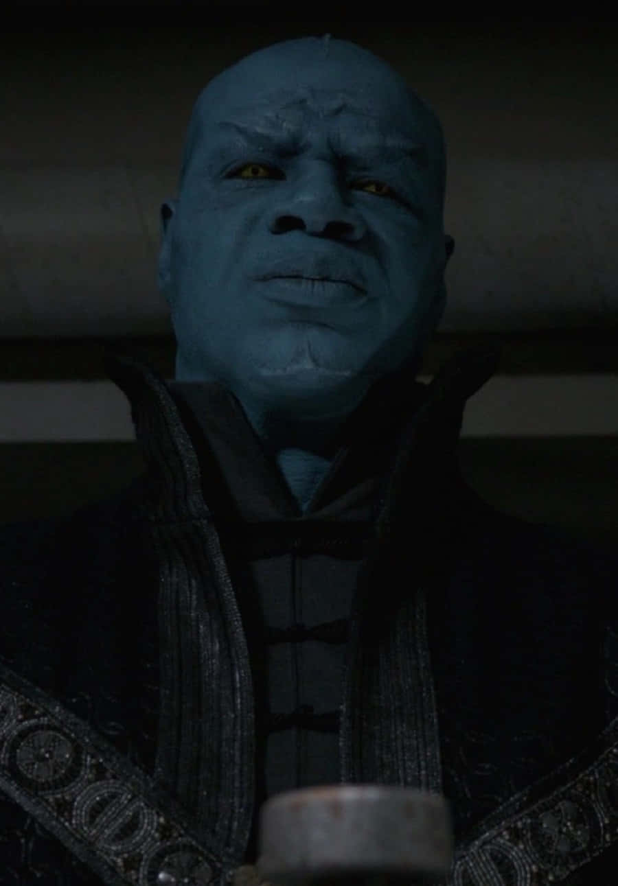 Kree 桌布 壁紙 — 一個藍皮膚的外星人，在光線昏暗、陰影重重的室內，用發光的黃色眼睛強烈地凝視著。