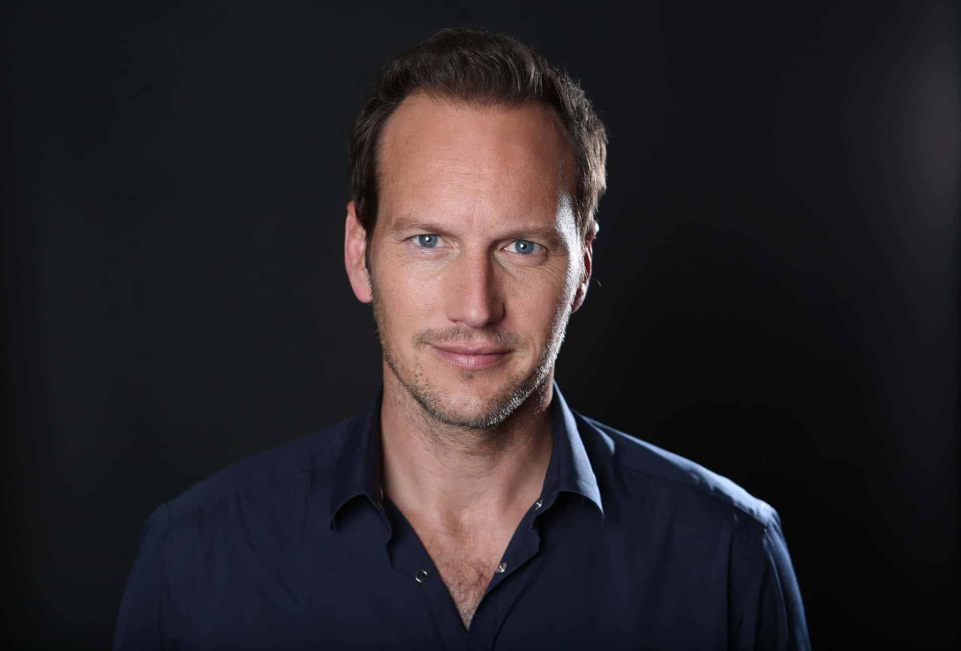 Patrick Wilson 桌布 壁紙 — 一個藍眼睛、短棕髮的男人，穿著深藍色襯衫，背景為黑色。