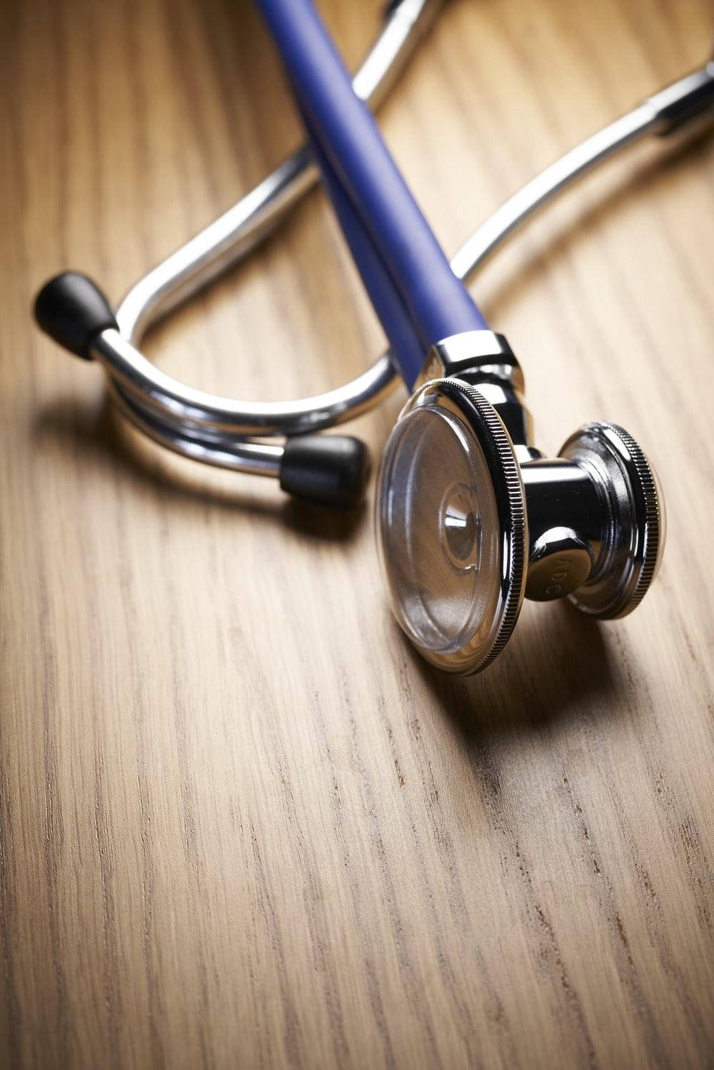 Stethoscope 桌布 壁紙 — 一個藍色和銀色的聽診器對角放置在溫暖的木質表面上，光線柔和。