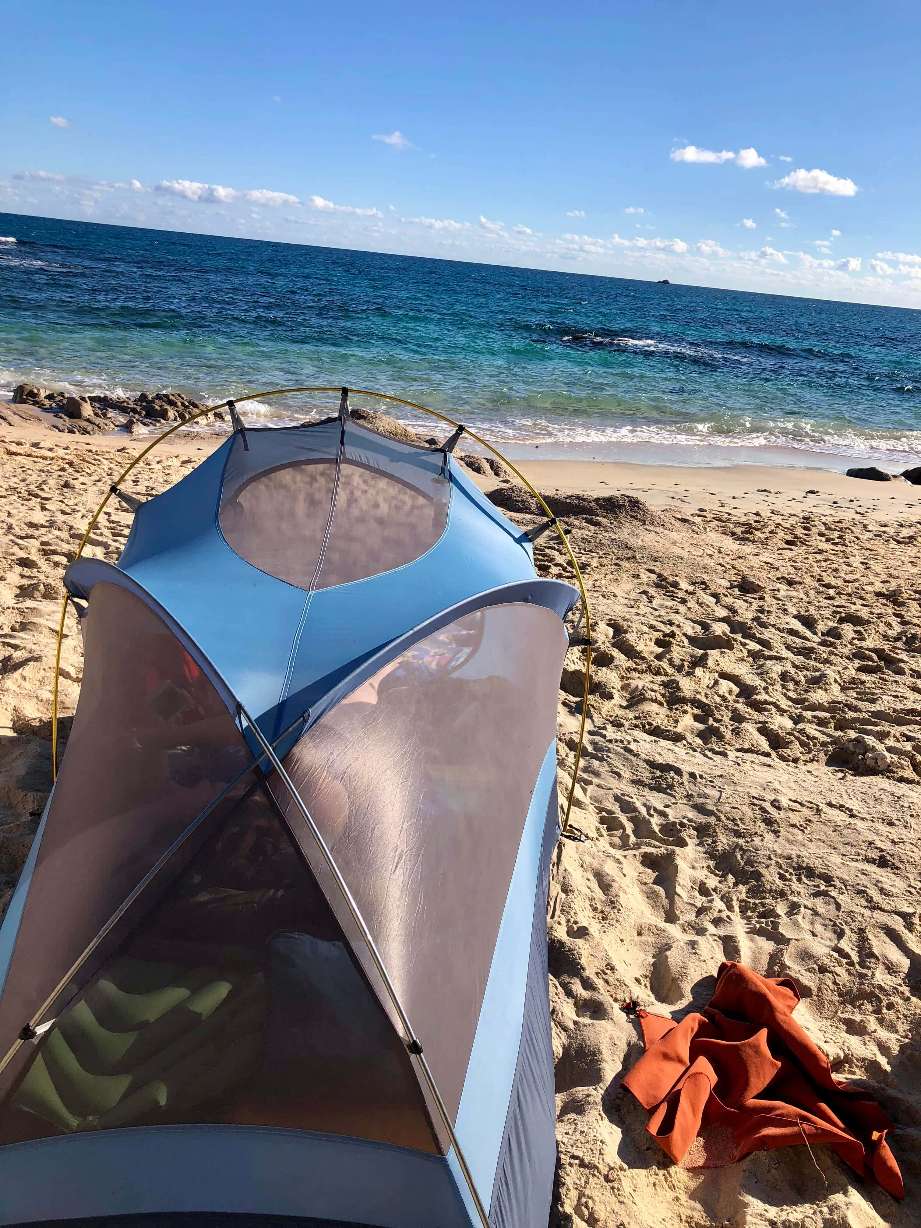 Beach Camping 桌布 壁紙 — 一個藍色帳篷搭建在沙灘上，附近有碧綠色的海浪拍打，天空清澈湛藍。