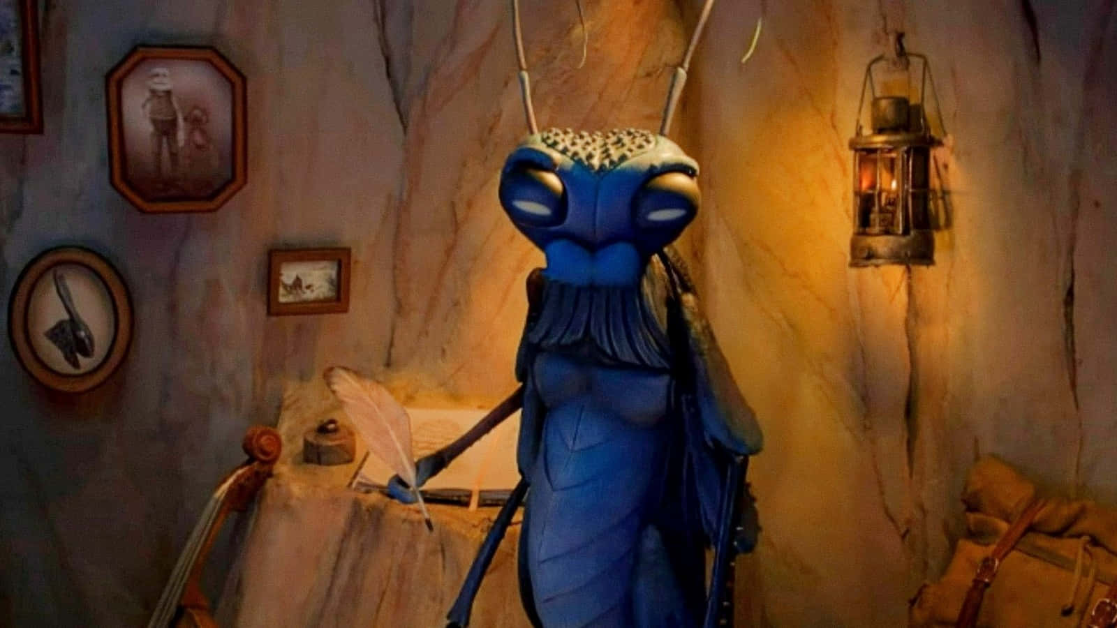 Guillermo Del Toro's Pinocchio 桌布 壁紙 — 一個藍色昆蟲狀角色站在一個溫暖照明的洞穴狀房間裡，房間裡有裱框圖片和一個掛著的燈籠。