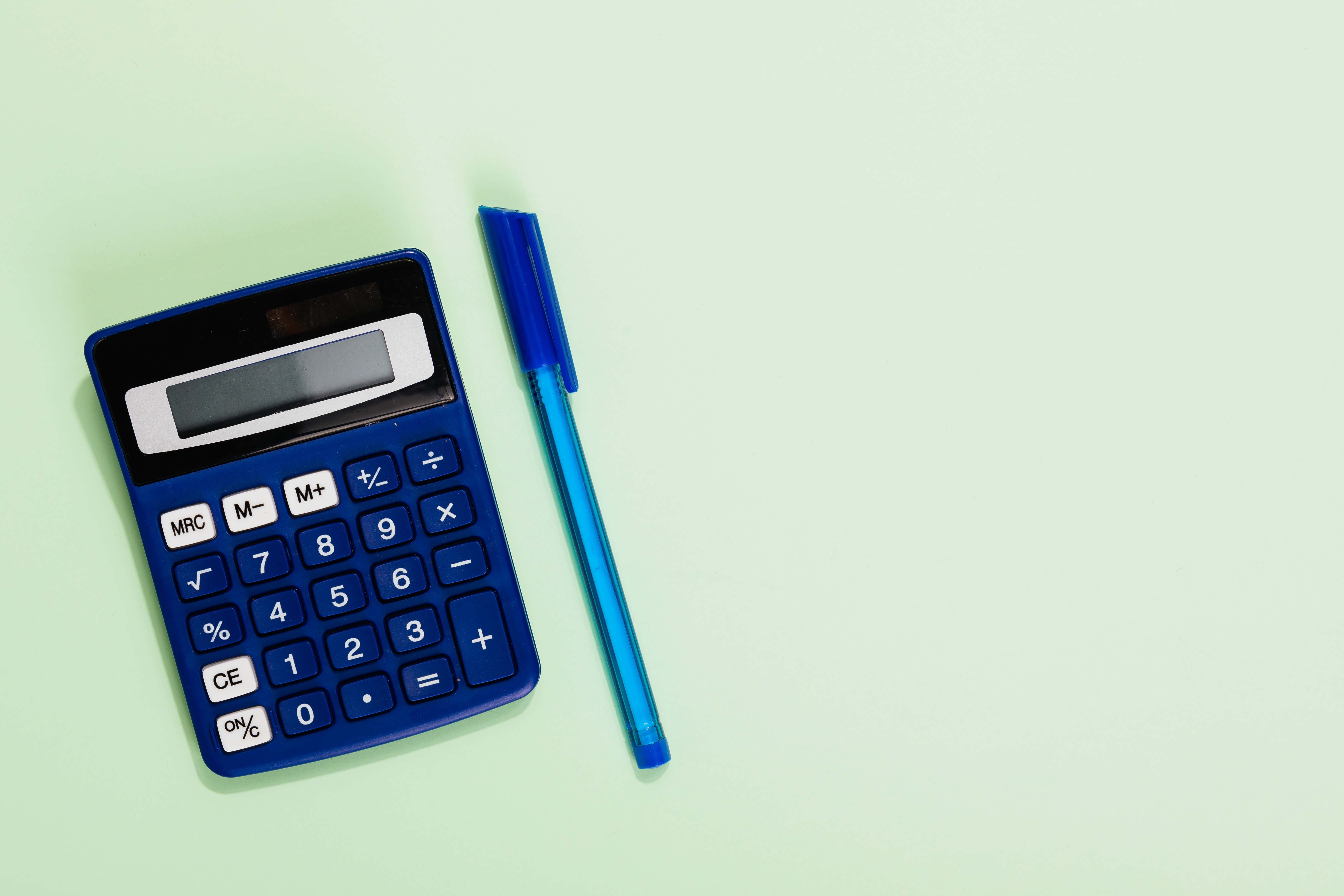 Calculator 桌布 壁紙 — 一個藍色計算機和一支筆放在柔軟的薄荷綠色表面上，構成極簡風格的平鋪構圖。