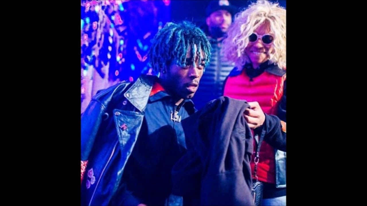 Lil Uzi Vert 桌布 壁紙 — 一個藍色辮子、身穿皮褸的男人，站在一個微笑、金色曲髮、戴太陽眼鏡的女人旁邊，在鮮豔的霓虹燈光下。