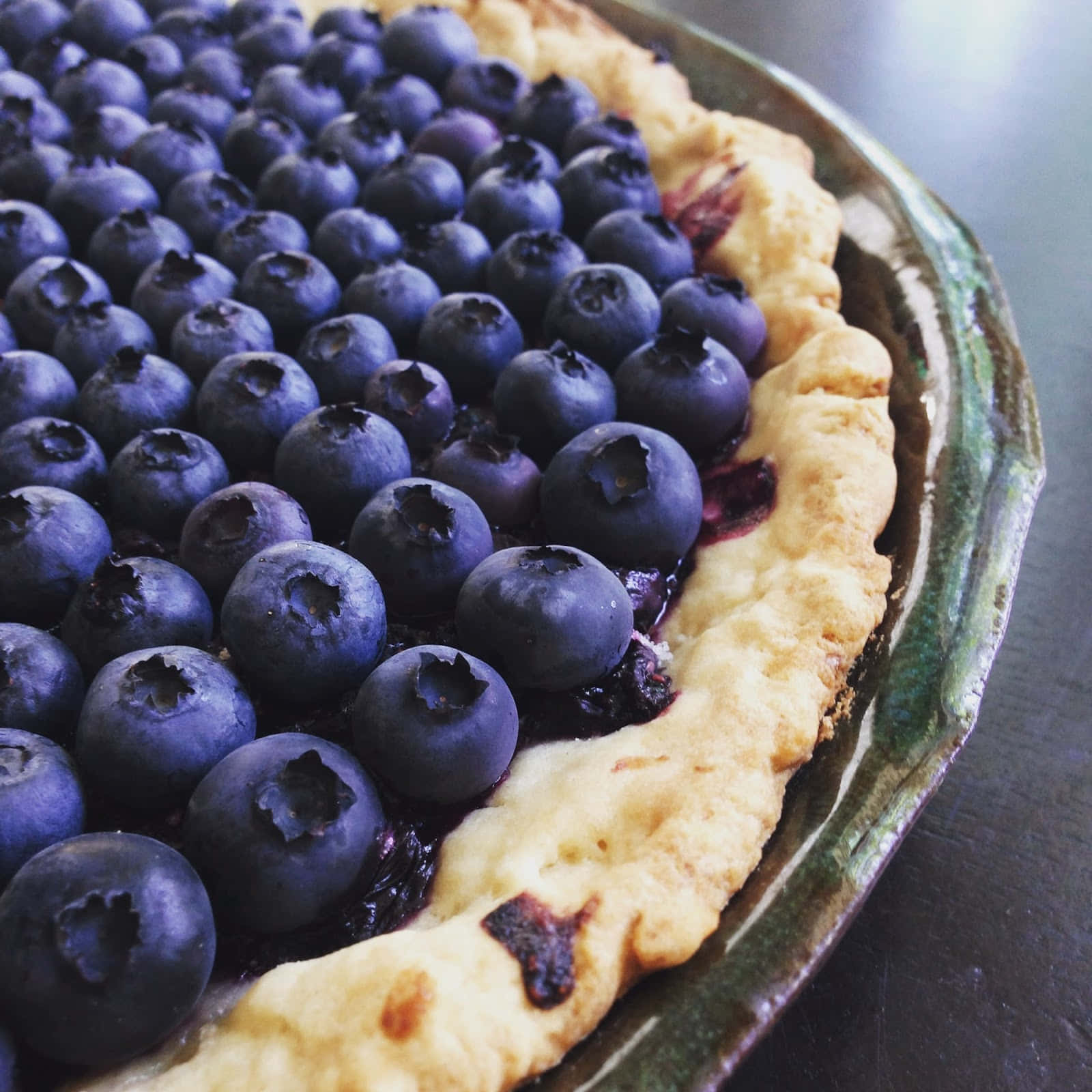 Blueberries Tart 桌布 壁紙 — 一個藍莓批的特寫，帶有閃亮嘅莓果同金黃色嘅批皮，放喺一個鄉村風格嘅陶瓷碟上。