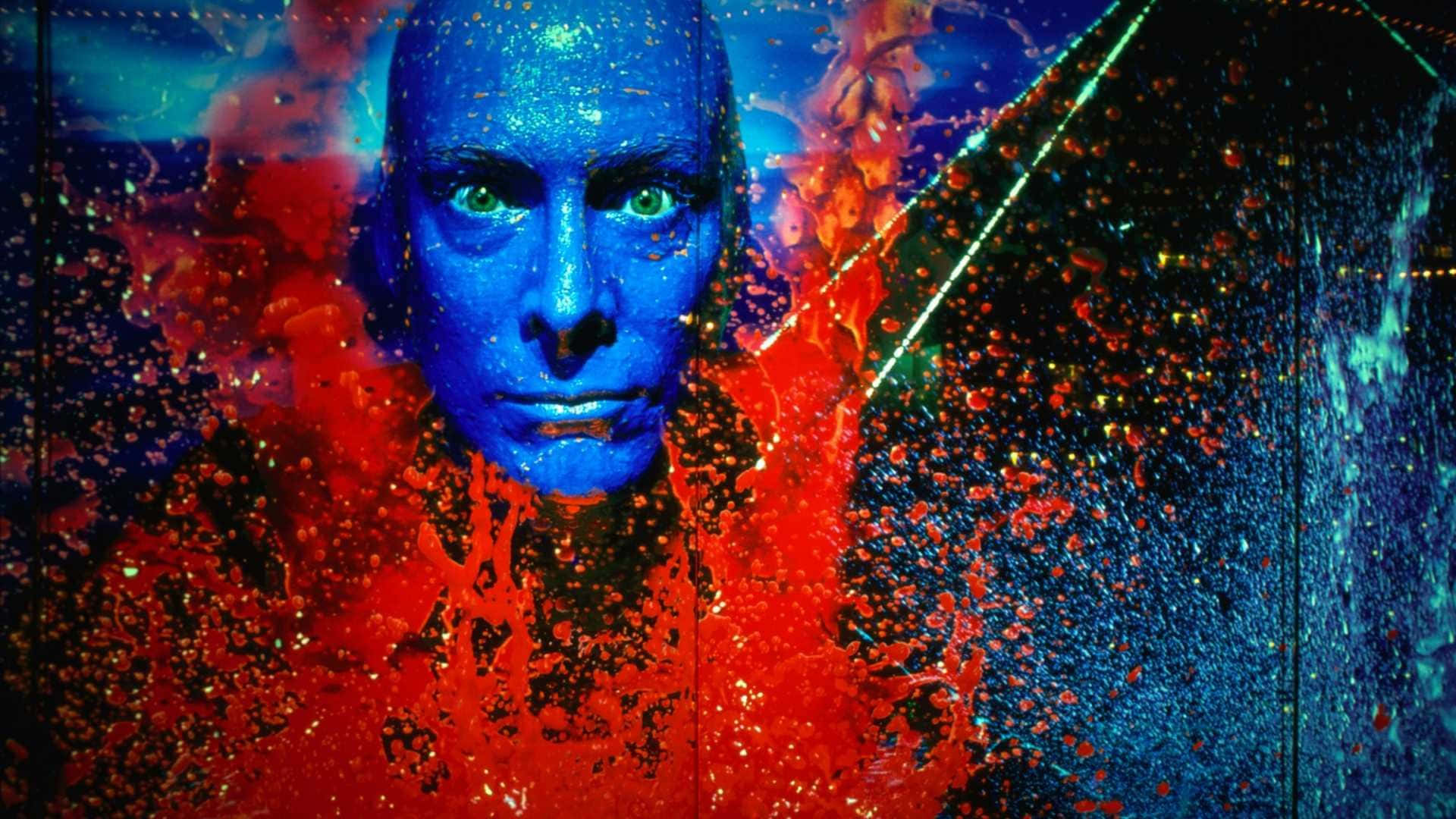 Blue Man Group 桌布 壁紙 — 一個藍面人物，綠色眼睛，透過火紅和電藍色的抽象顏料和光爆炸凝視。