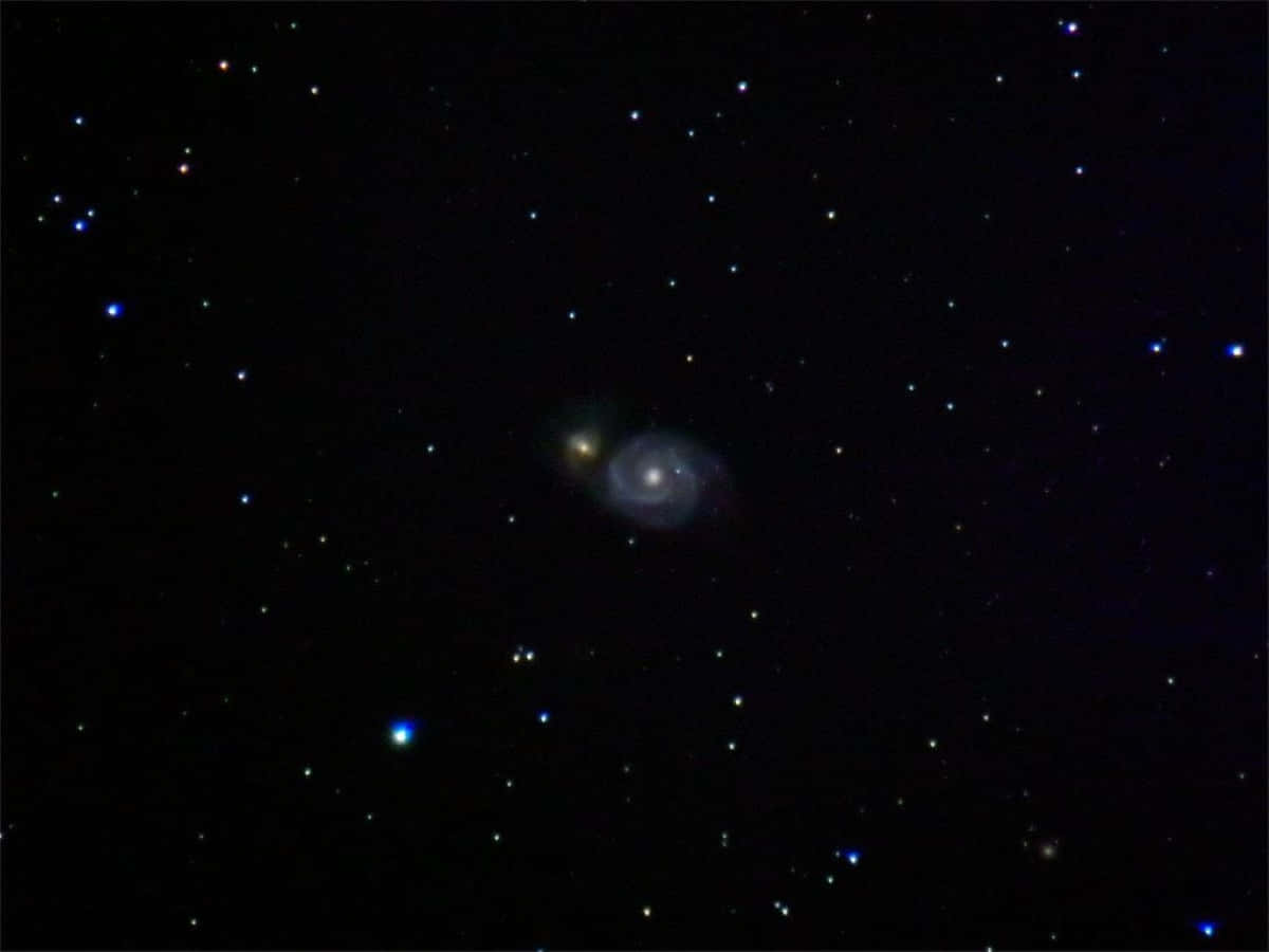 Whirlpool Galaxy 桌布 壁紙 — 一個螺旋星系在一片閃爍星場中柔和地發光，背景是深邃的黑色宇宙虛空。