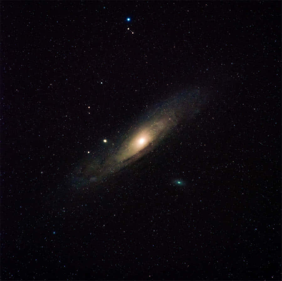 Elliptical Galaxy 桌布 壁紙 — 一個螺旋星系在深空中散佈著藍色和綠色星星的星場中溫暖地發光。