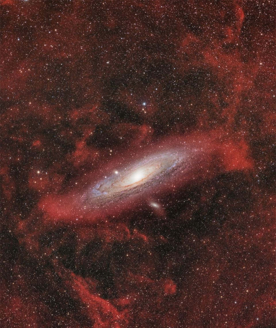 Interstellar Cloud 桌布 壁紙 — 一個螺旋星系發出明亮白色核心和旋轉臂的光芒，背景是深紅色的宇宙雲和散落的星星。