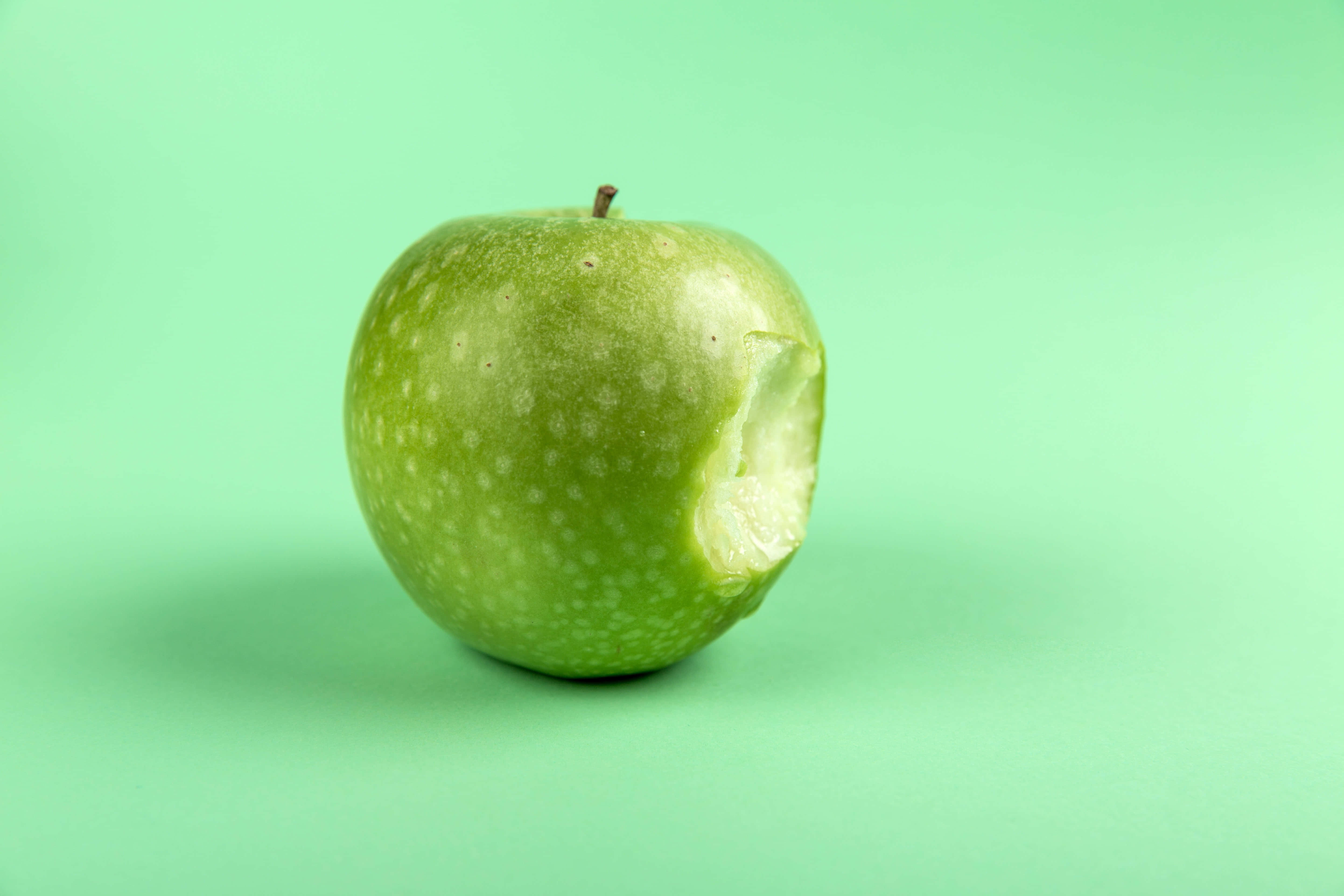 Summer Fruits 桌布 壁紙 — 一個被咬咗一啖嘅青蘋果，上面有白色斑點，放喺純薄荷綠色背景上。
