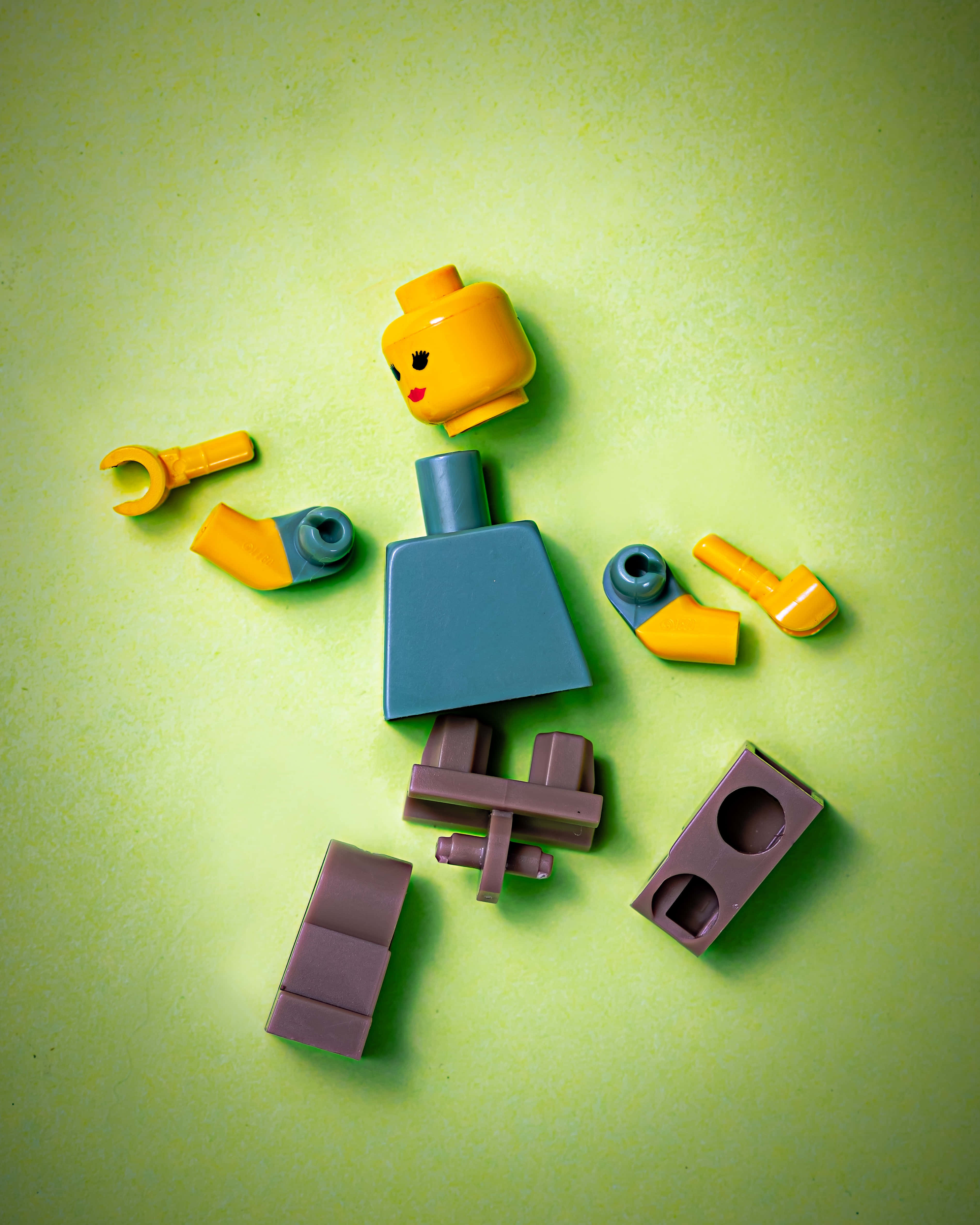 hurt 桌布 壁紙 — 一個被拆解的LEGO人仔，黃色頭部和藍色身體，散落在鮮豔的綠色背景上。