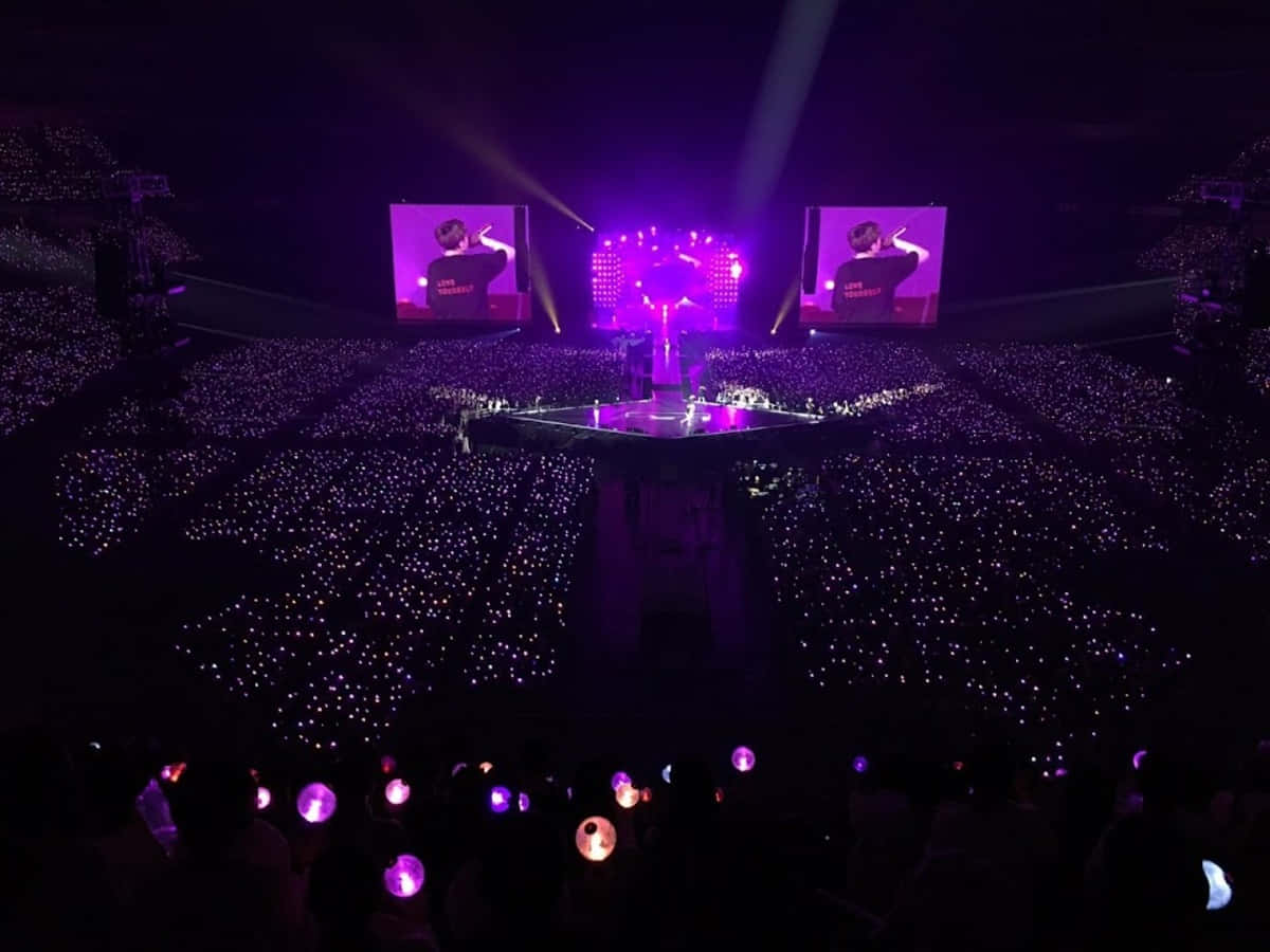Bts Stage 桌布 壁紙 — 一個被紫色燈光籠罩的演唱會舞台，粉絲們手持發光棒，創造出一片星海。
