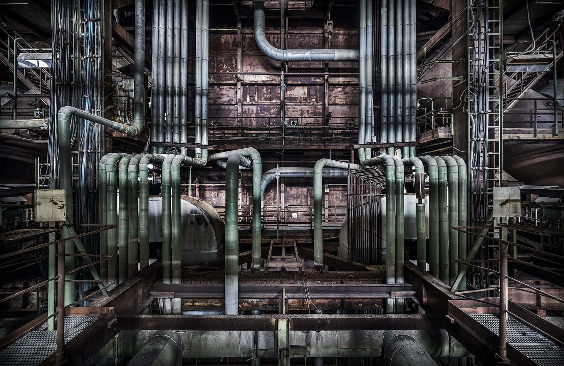Manufacturing 桌布 壁紙 — 一個被遺棄的工業廠房，在昏暗燈光下，生鏽的管道和腐朽的金屬結構散發著詭異的美感。