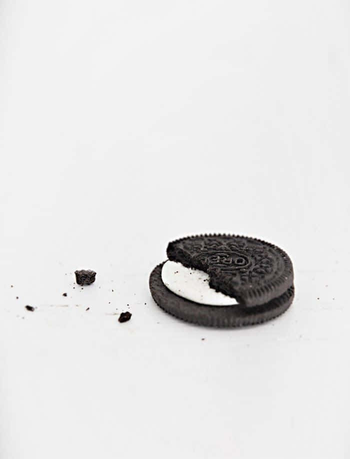 Minimalist Photography 桌布 壁紙 — 一個被部分食用的Oreo曲奇，碎屑散落在純白表面上。