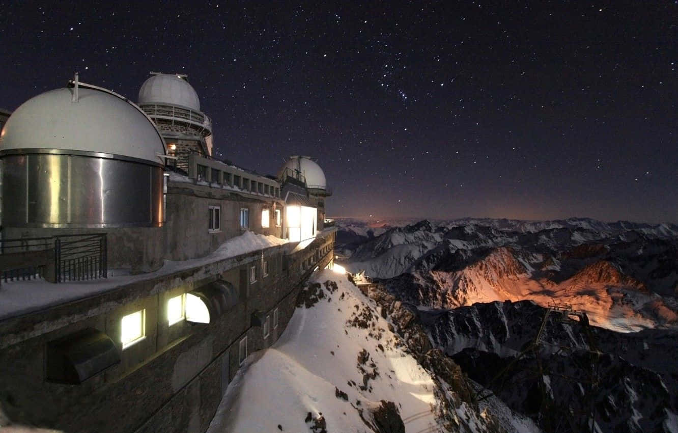 Space Observation 桌布 壁紙 — 一個被雪覆蓋的山頂天文台在繁星點點的夜空下閃耀，俯瞰著廣闊的阿爾卑斯山谷。