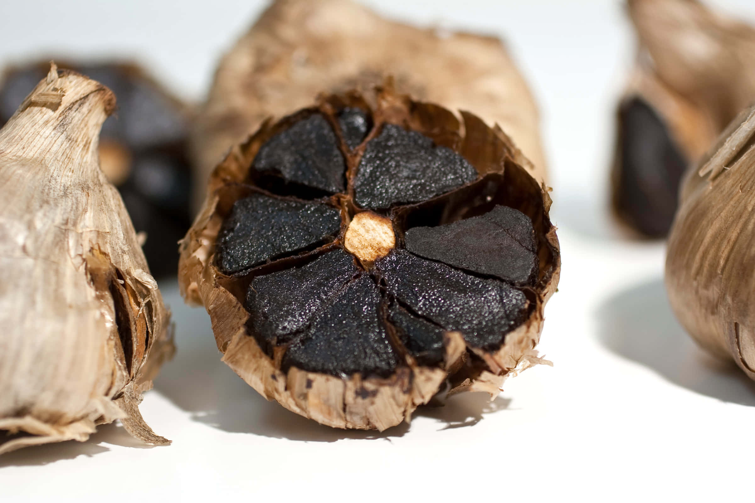 Black Garlic 桌布 壁紙 — 一個裂開的黑蒜頭的特寫，在明亮的白色背景上顯露出光澤的深色蒜瓣。