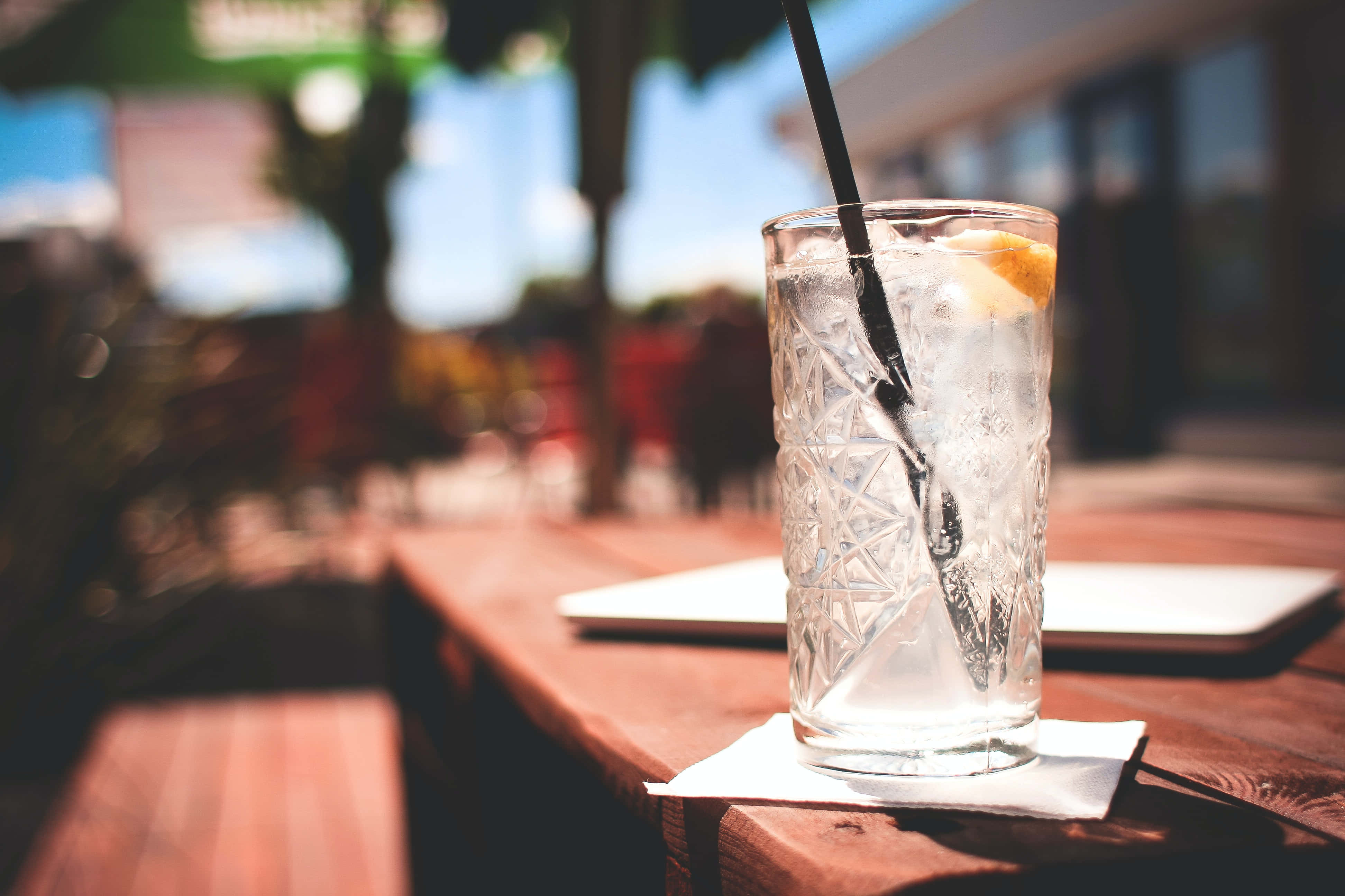 Summer Drinks 桌布 壁紙 — 一個裝滿冰塊和柑橘裝飾的水晶杯放在木桌上，沐浴在明亮的陽光下。