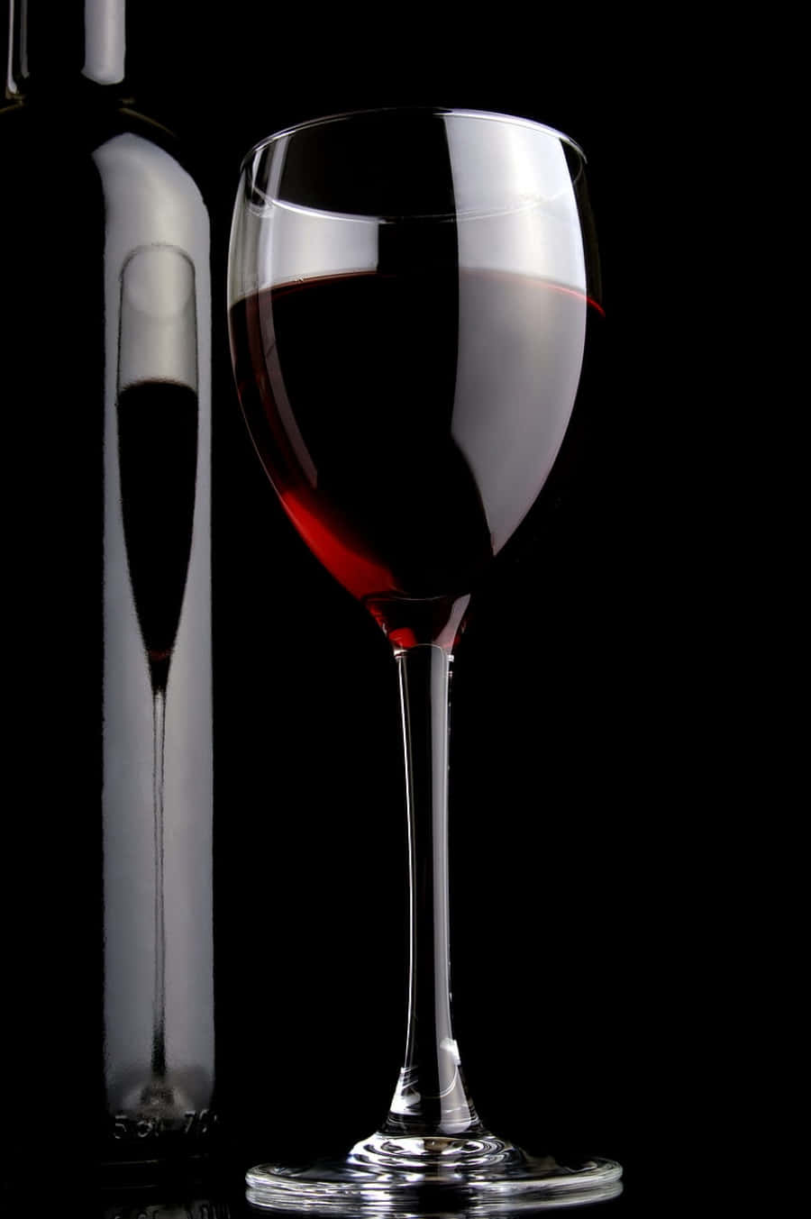 Black Wine 桌布 壁紙 — 一個裝滿深紅酒的水晶酒杯放在酒瓶旁邊，背景是純黑色。