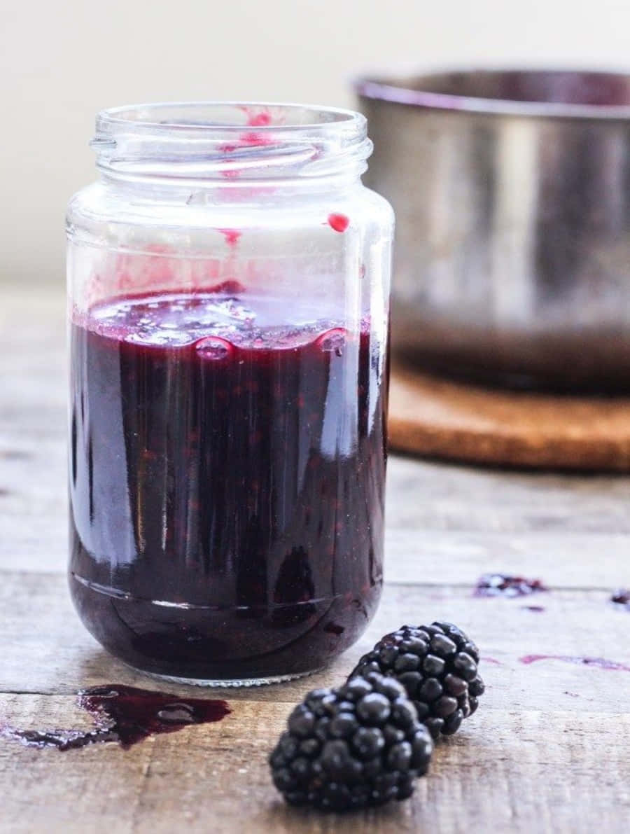 Blackberry Jam 桌布 壁紙 — 一個裝滿濃郁深紫色黑莓果醬的玻璃罐放在質樸的木桌上，旁邊有新鮮的黑莓。