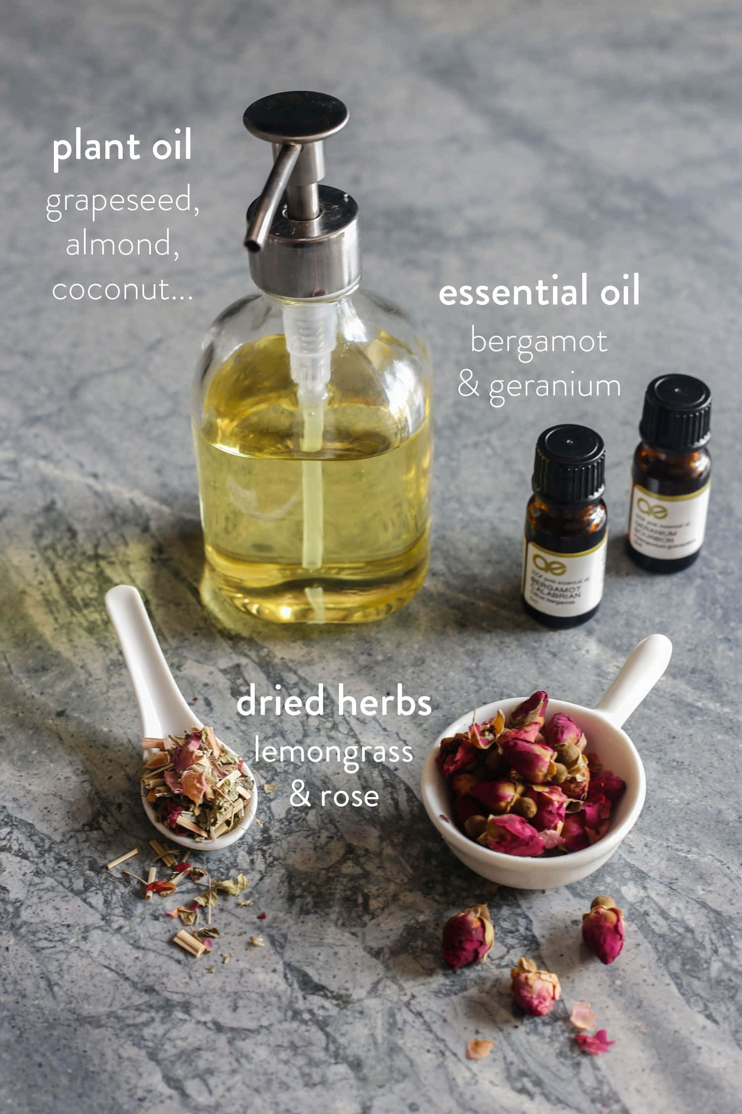 Rose Oil 桌布 壁紙 — 一個裝滿金色油的玻璃皂液器，旁邊放著小瓶精油和裝有乾檸檬草和玫瑰花瓣的碗，置於灰色石面上。