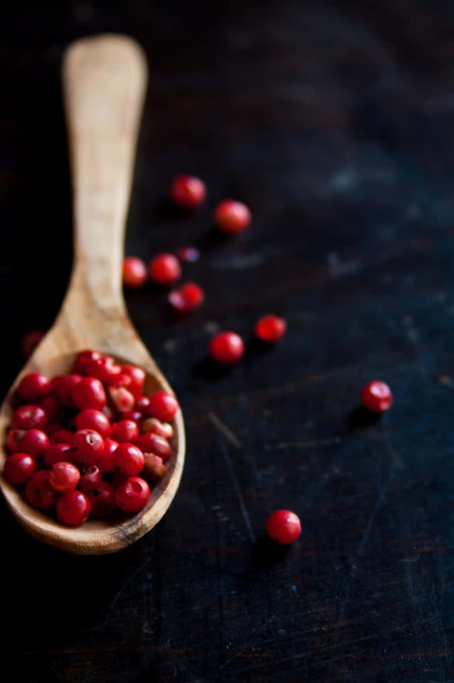Pink Peppercorn 桌布 壁紙 — 一個裝滿鮮紅色胡椒粒的木勺放在深色鄉村風格的表面上，周圍散落著漿果。