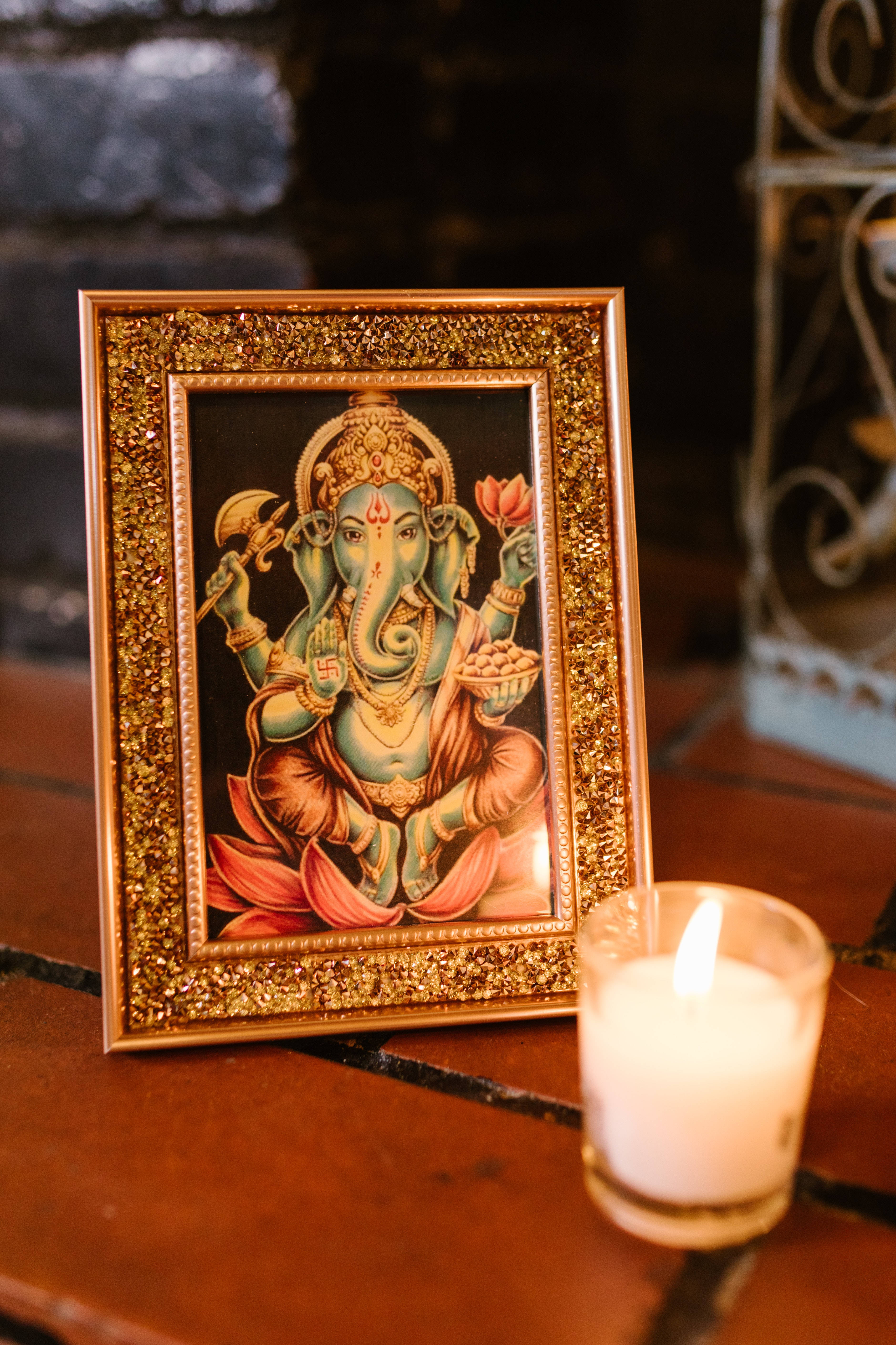 Ganesh 桌布 壁紙 — 一個裝裱的象神畫像，旁邊有一根點燃的蠟燭放在木質表面上。