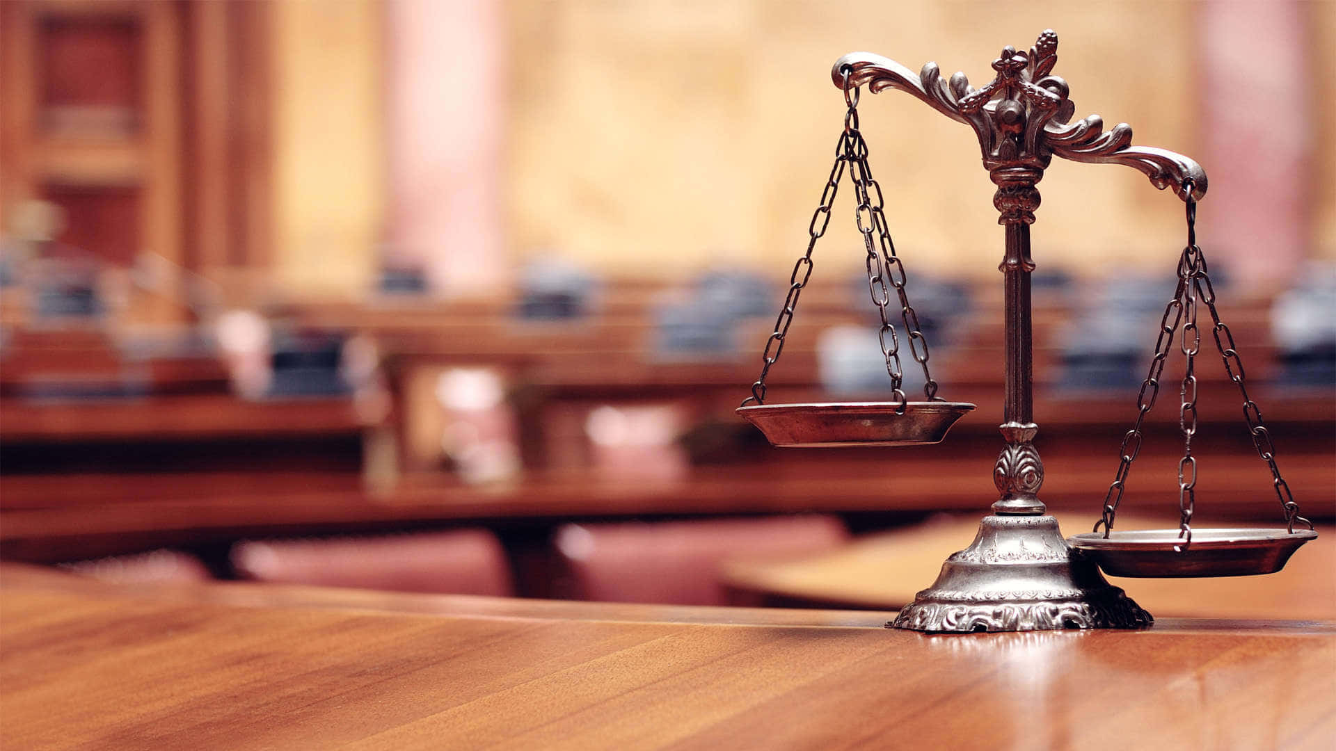 Law 桌布 壁紙 — 一個裝飾性的青銅正義天秤放在一張拋光木製法庭桌子的中央，後面是模糊的座位排。