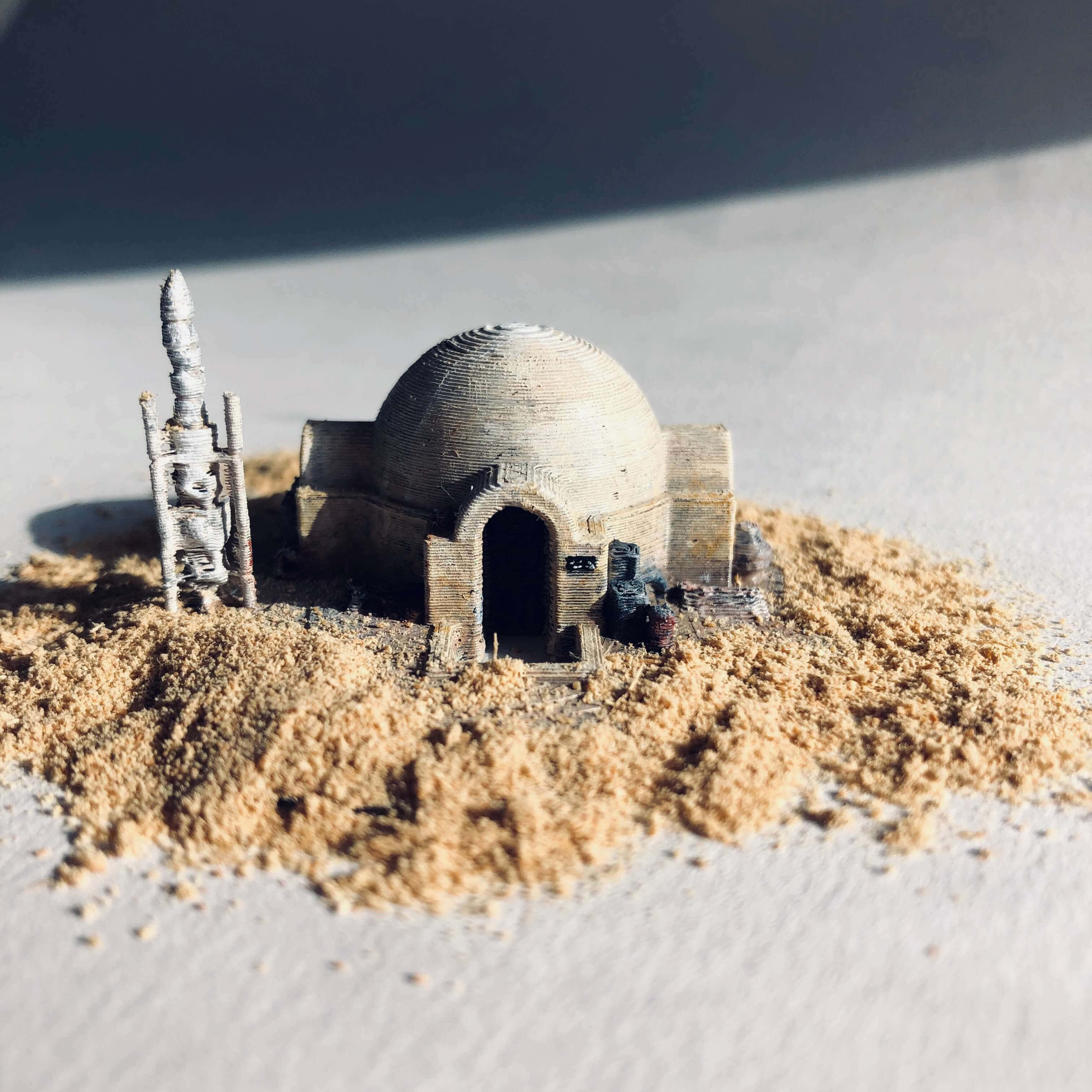 Tatooine 桌布 壁紙 — 一個詳細的3D打印沙漠圓頂房屋模型，帶有高塔，坐落在沙堆上，處於明亮的陽光下。