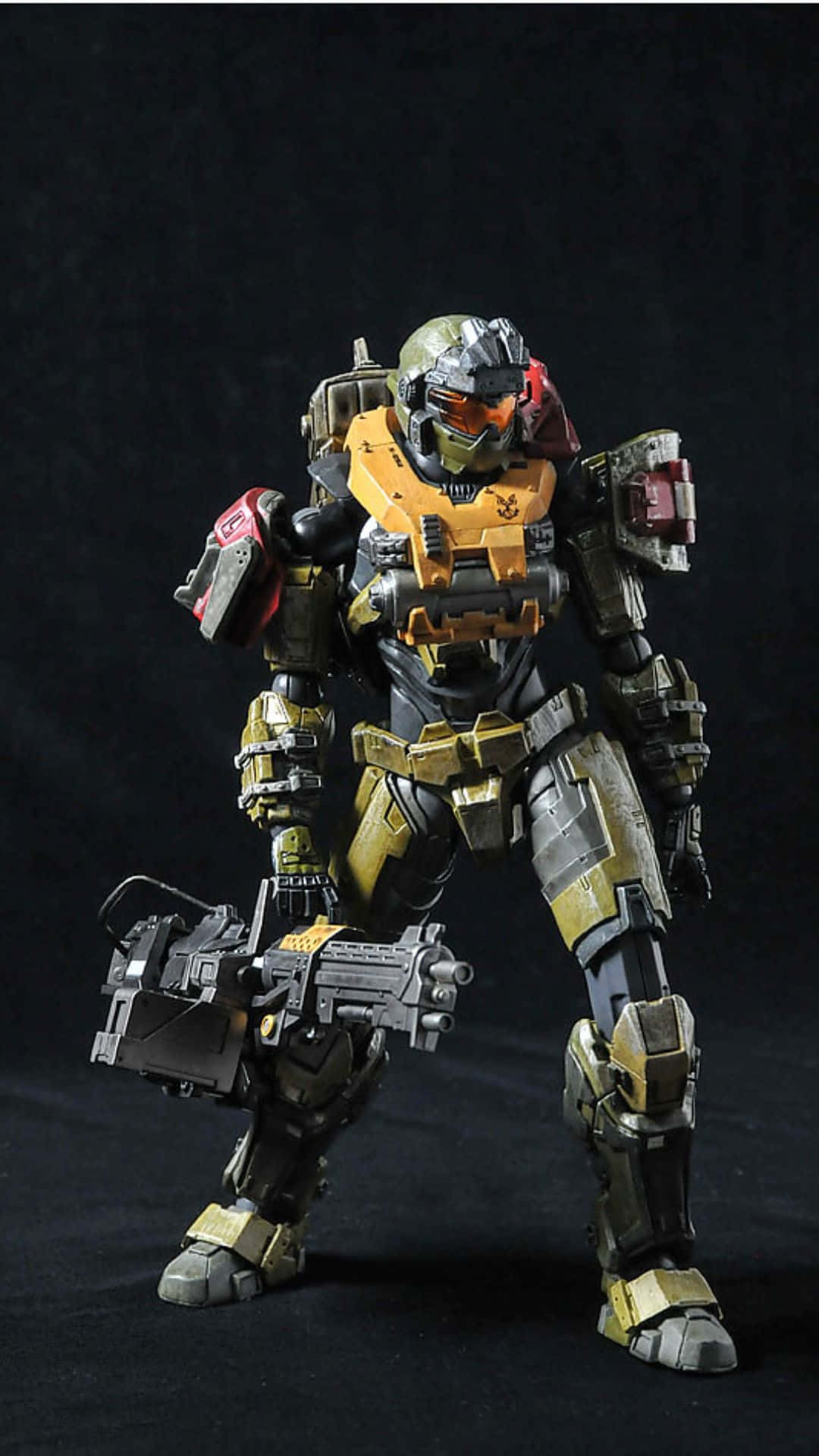 Jorge-052 桌布 壁紙 — 一個詳細的Halo Spartan動作人偶，身穿金色和黑色盔甲，在黑暗背景下手持重型武器擺出姿勢。