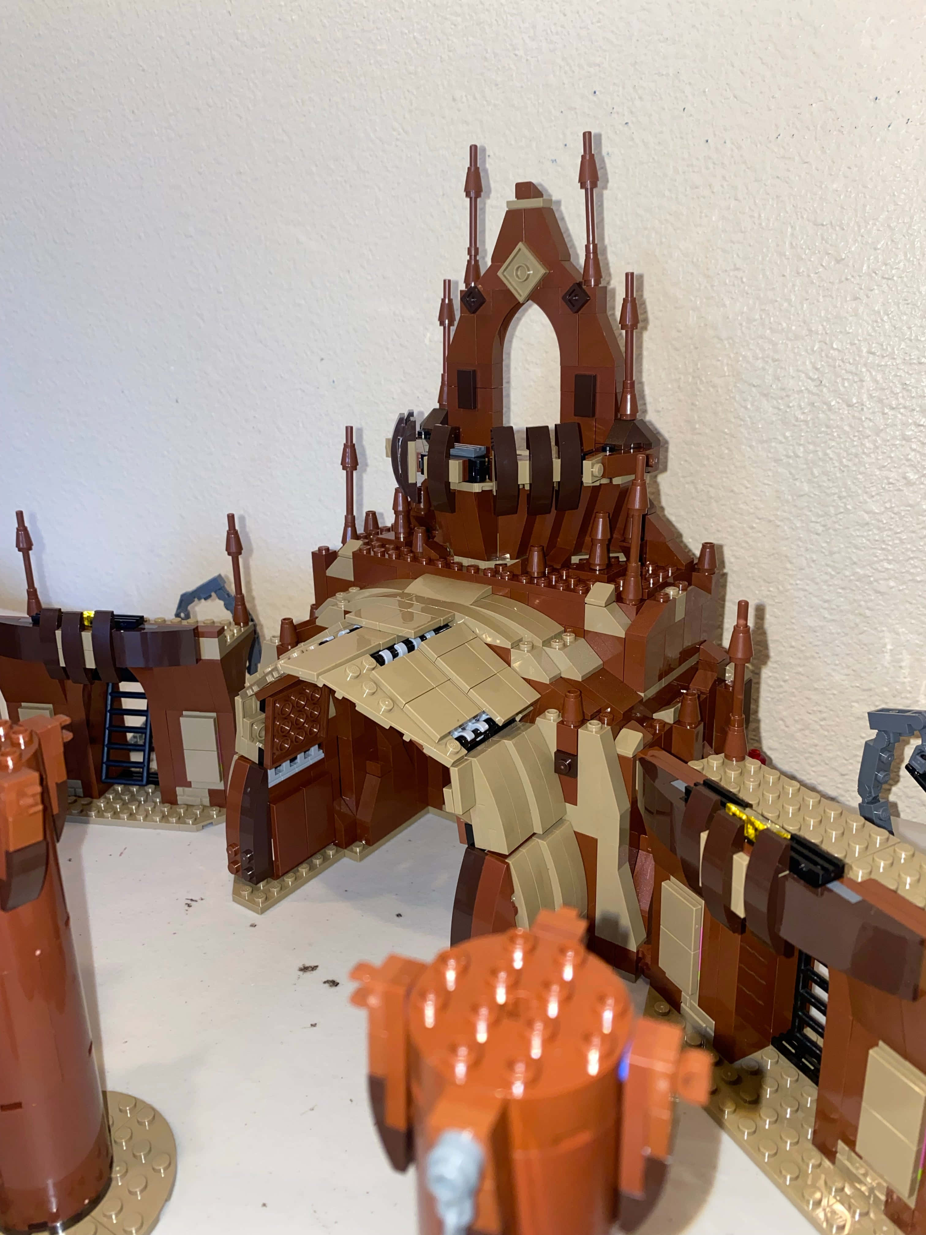 The Geonosian Arena 桌布 壁紙 — 一個詳細的LEGO城堡模型，由棕色和米色磚塊製成，放在白色表面上，背景是純白牆壁。