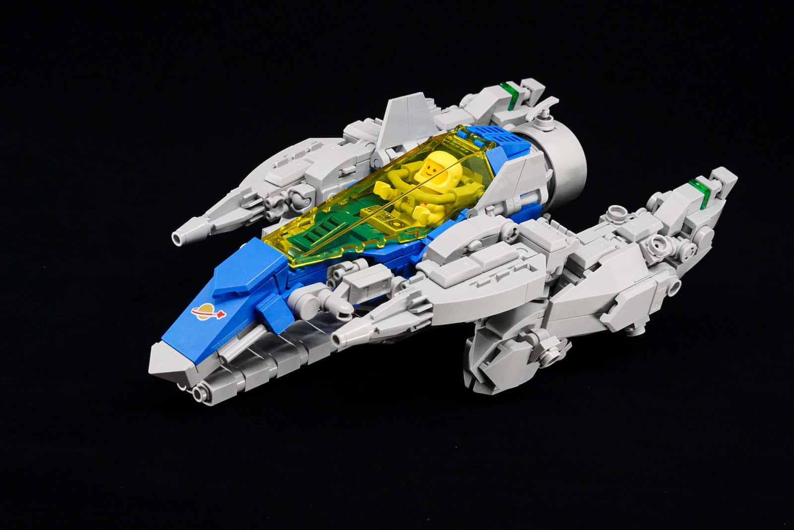 太空船 桌布 壁紙 — 一個詳細的LEGO太空船，帶有藍色和灰色面板，以及一個在透明駕駛艙內的黃色飛行員，背景為黑色。