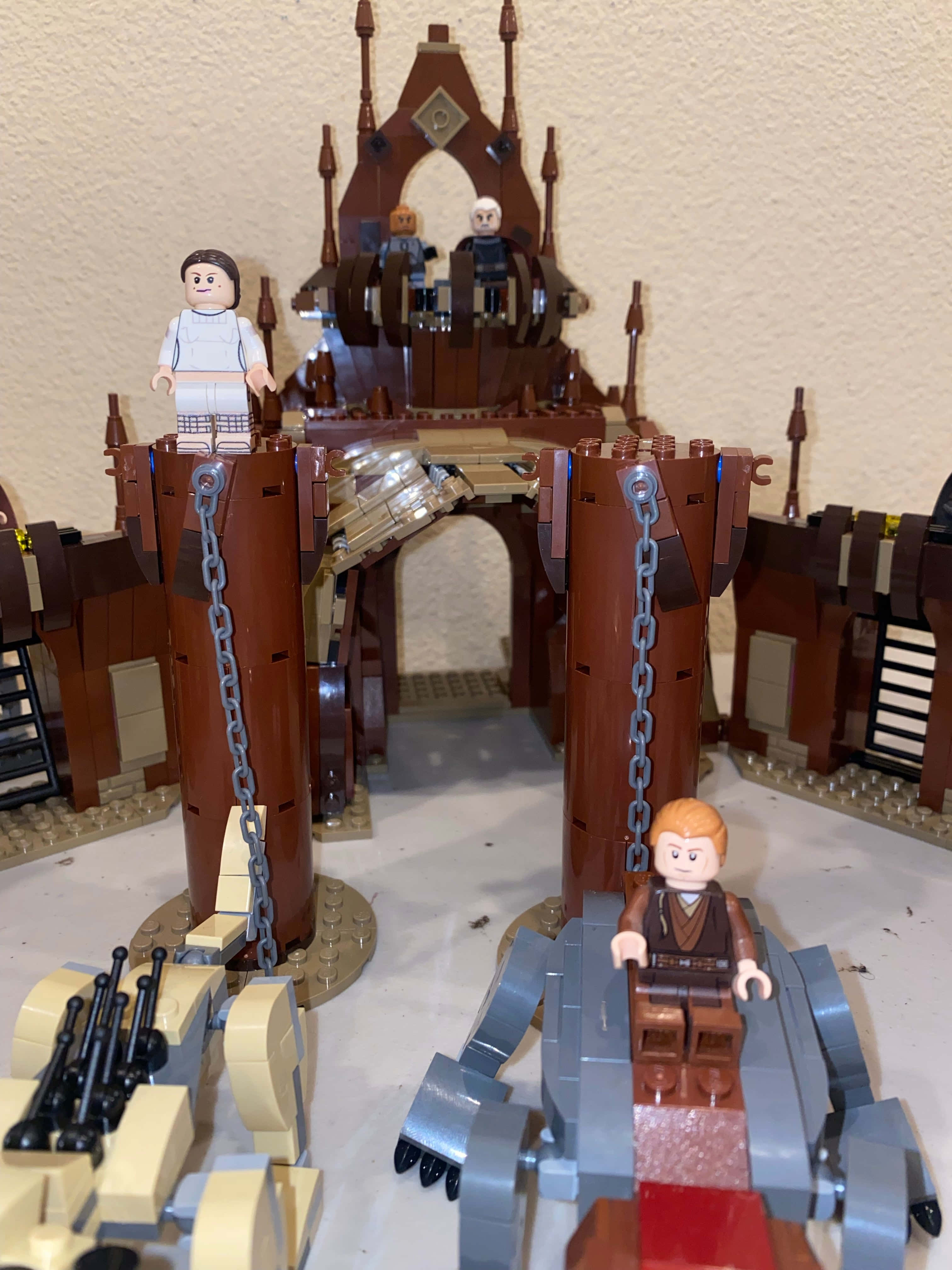 The Geonosian Arena 桌布 壁紙 — 一個詳細的LEGO星際大戰套裝， featuring 人仔在棕色堡壘上，配有鏈條升降機和前景中的飛車。