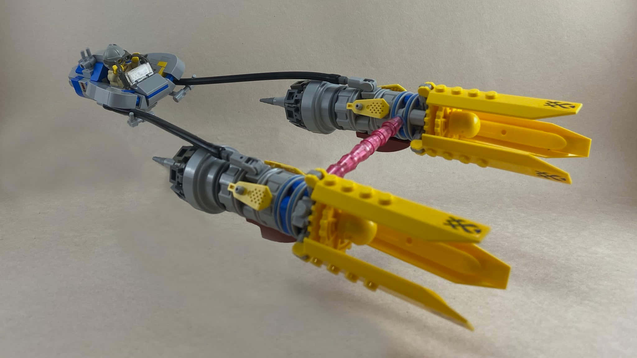 Podracing 桌布 壁紙 — 一個詳細的LEGO模型，描繪了一艘未來風格的太空船，帶有黃色機翼和灰色引擎，背景為純米色。