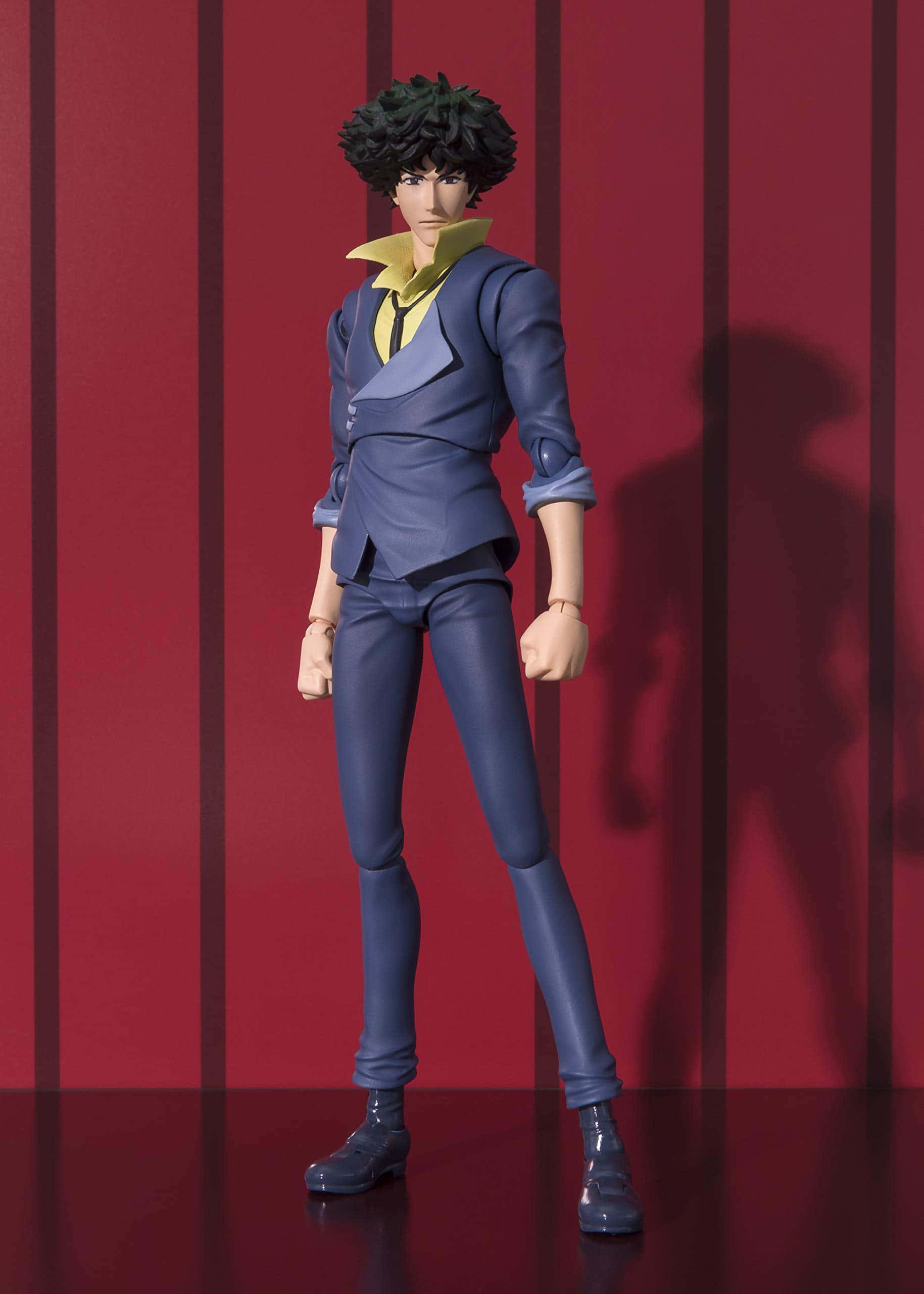 Spike Spiegel 桌布 壁紙 — 一個詳細的動漫人偶，黑色捲髮男子穿著藍色西裝和黃色襯衫，自信地站在紅色條紋牆前。