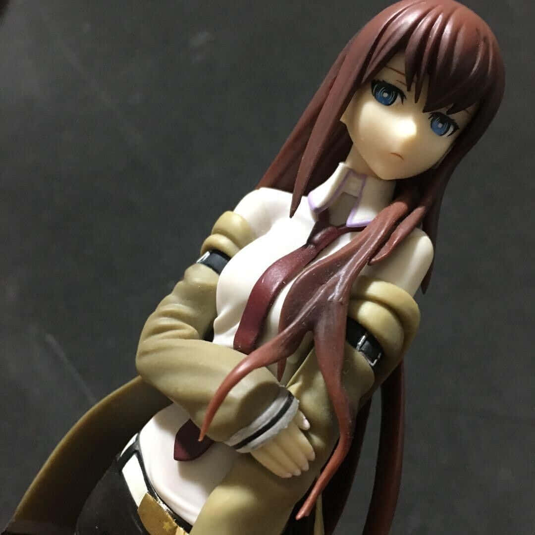 kurisu makise 桌布 壁紙 — 一個詳細的動漫人物模型，描繪一位棕色頭髮、藍色眼睛的女孩，穿著米色外套和紅色領帶，雙臂交叉，背景為深灰色。