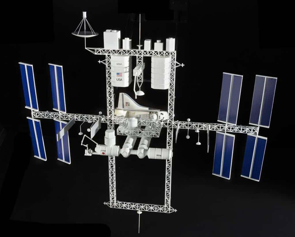 International Space Station 桌布 壁紙 — 一個詳細的國際太空站模型，帶有藍色太陽能板和白色模組，背景為黑色。