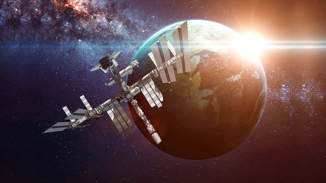 Satellite Technology 桌布 壁紙 — 一個詳細的太空站繞地球運行，太陽從行星彎曲的地平線升起，背景是繁星點點的星系。