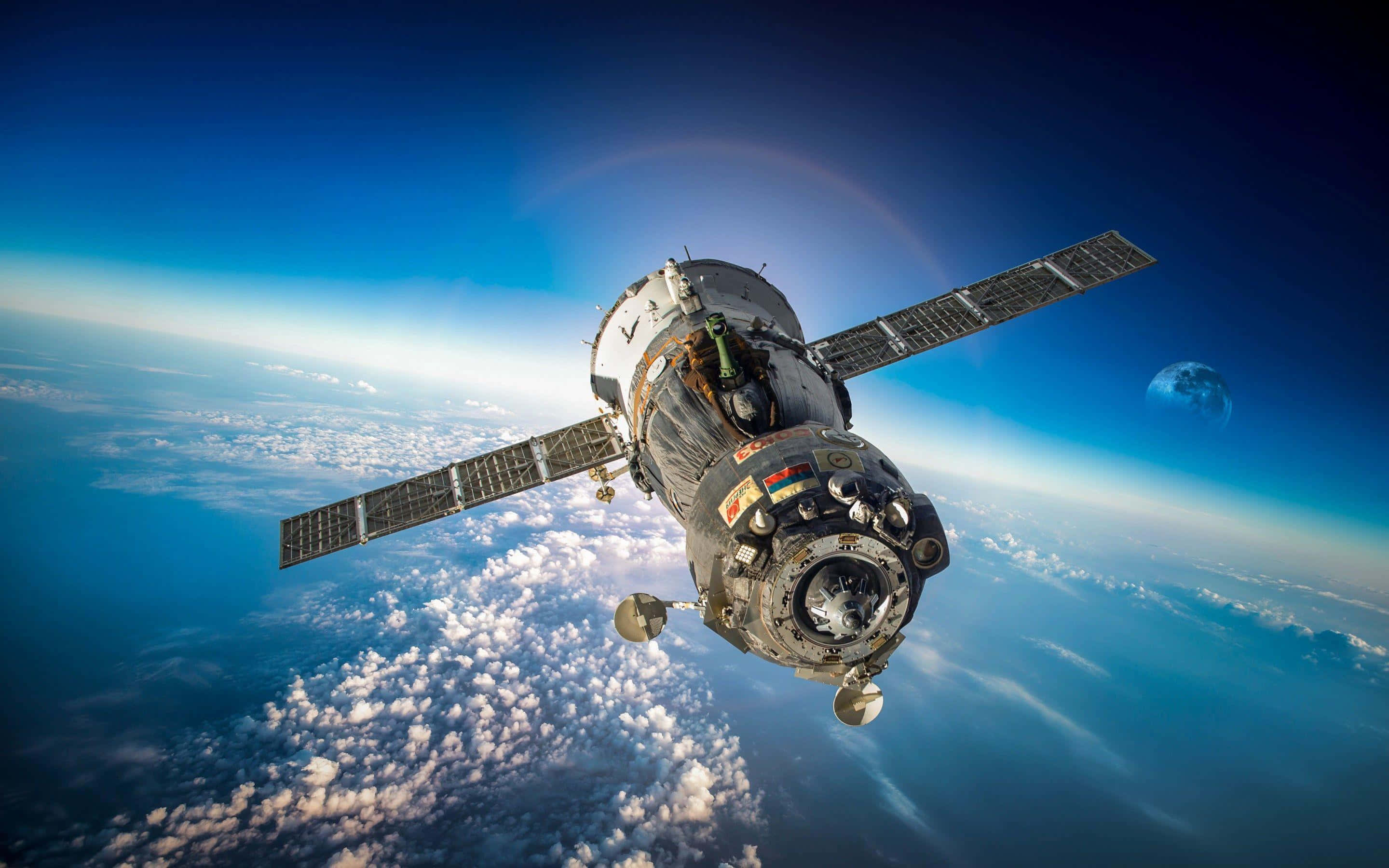 Satellite 桌布 壁紙 — 一個詳細的太空站繞地球運行，太陽能板展開，背景是藍色的雲層和彎曲的地平線。