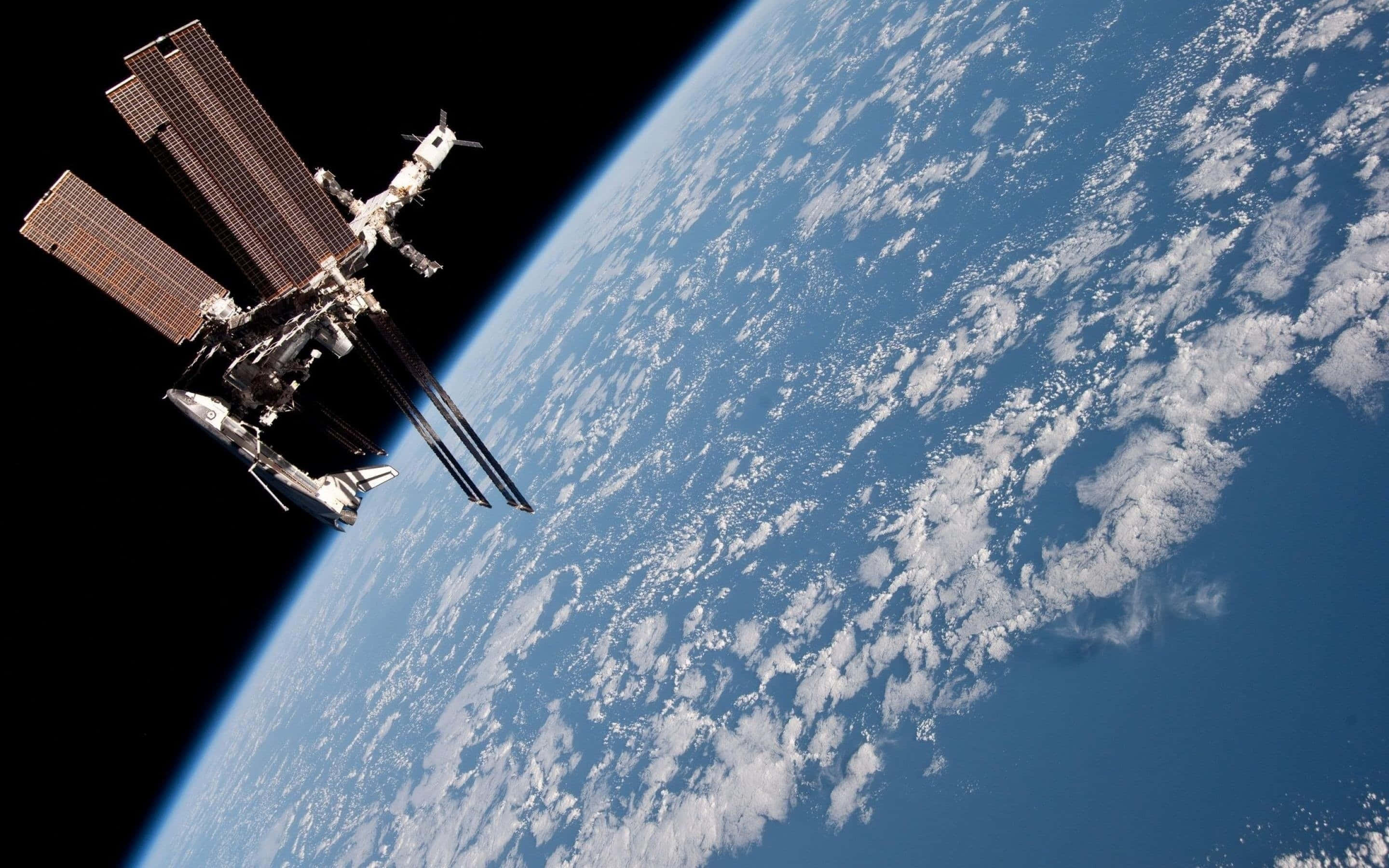 Iss 桌布 壁紙 — 一個詳細的太空站繞地球運行，展示其太陽能電池板，背景是地球藍白相間、雲層覆蓋的曲線。