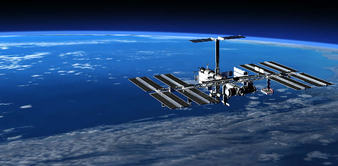 International Space Station 桌布 壁紙 — 一個詳細的太空站繞地球運行，展示太陽能電池板和模組，背景是藍色行星和白色雲層。