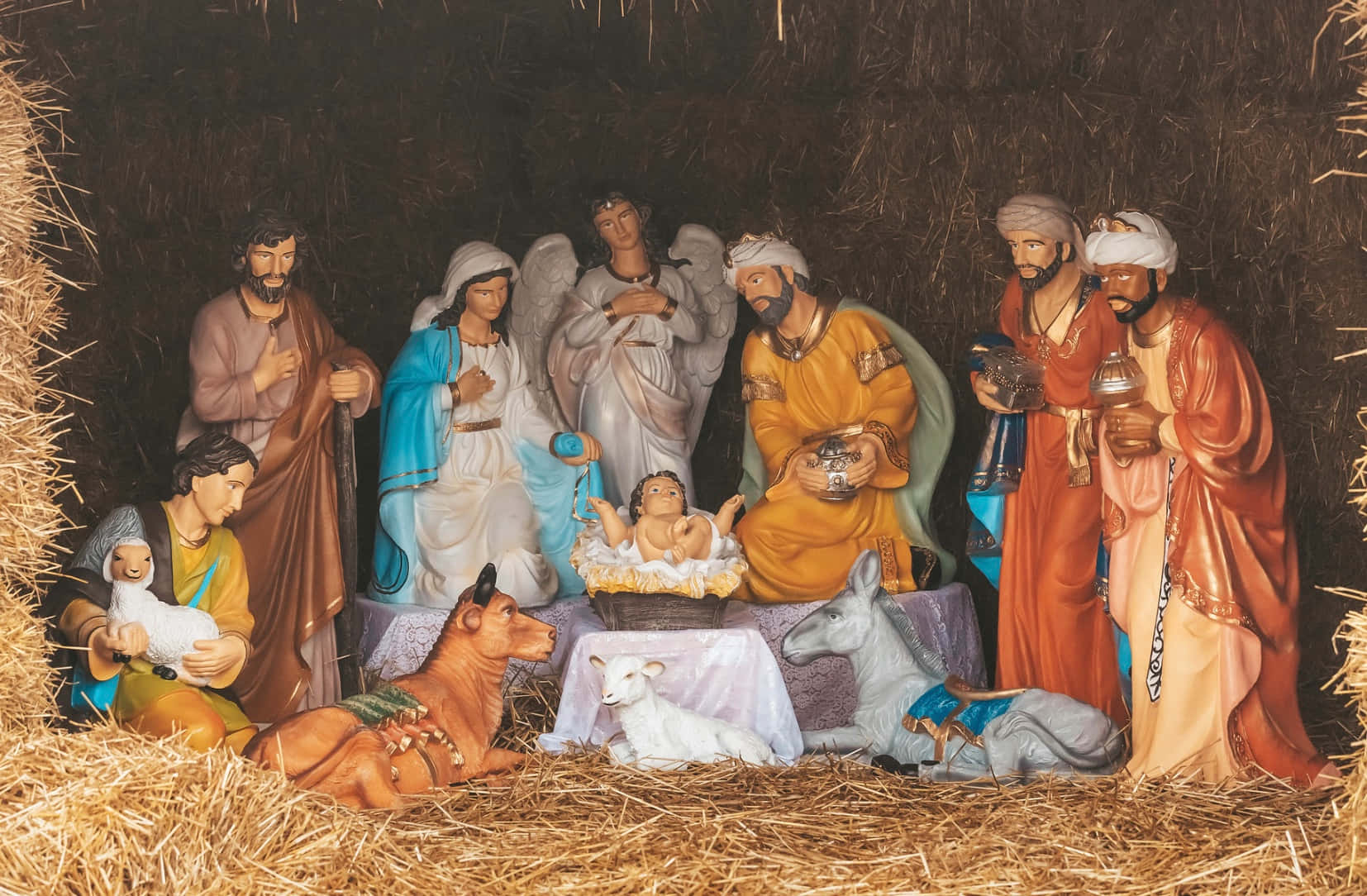 Nativity Scene 桌布 壁紙 — 一個詳細的耶穌誕生場景，有瑪利亞、約瑟、嬰兒耶穌、天使、牧羊人、智者及動物在一個充滿稻草的馬廄中的雕像。
