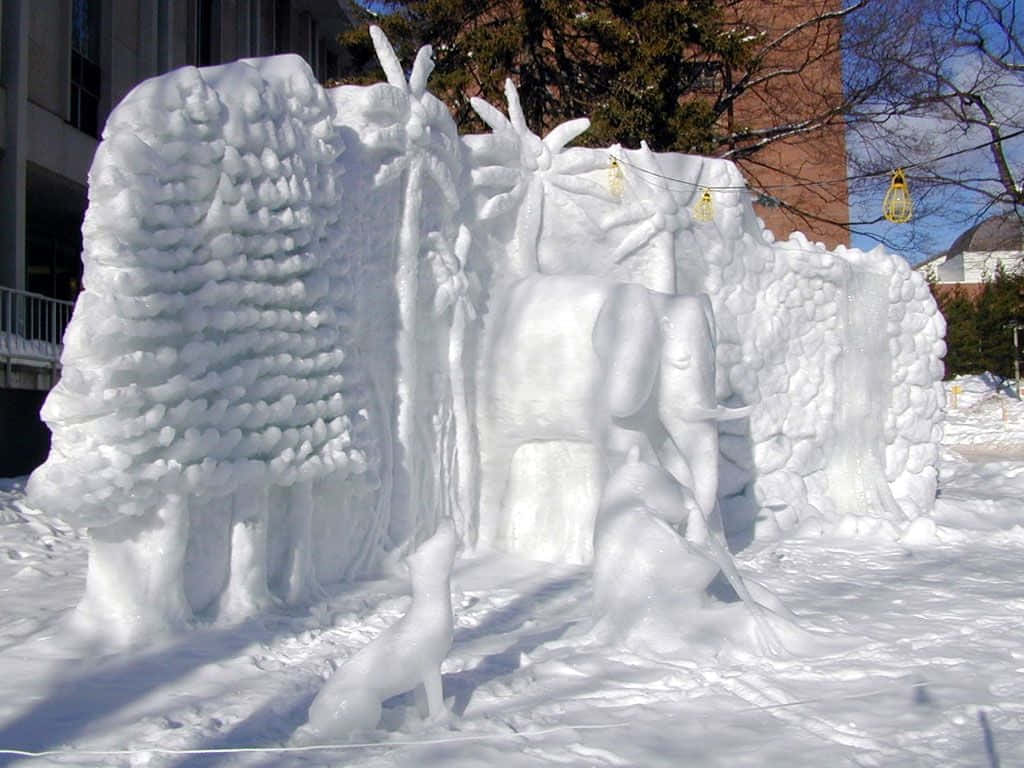 Ice Sculpture 桌布 壁紙 — 一個詳細的雪雕，在明亮的日光下，大象和狐狸置身於有紋理的雪牆之間。