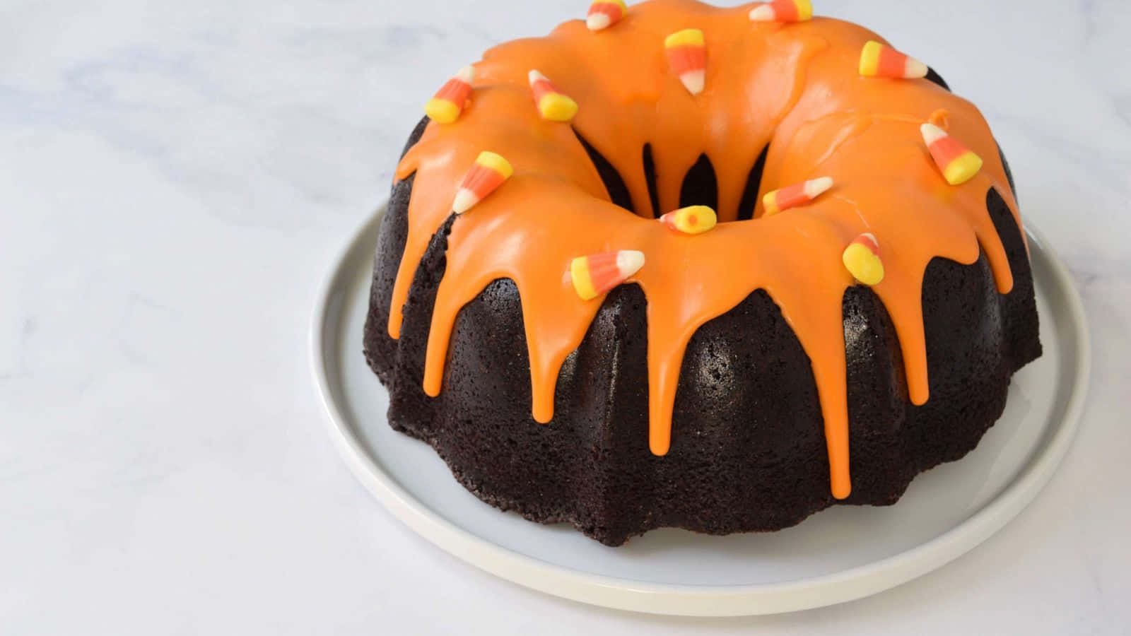 Halloween Cake 桌布 壁紙 — 一個豐富的朱古力環形蛋糕，淋上充滿活力的橙色糖霜，並在白色碟子上放上糖果粟米。